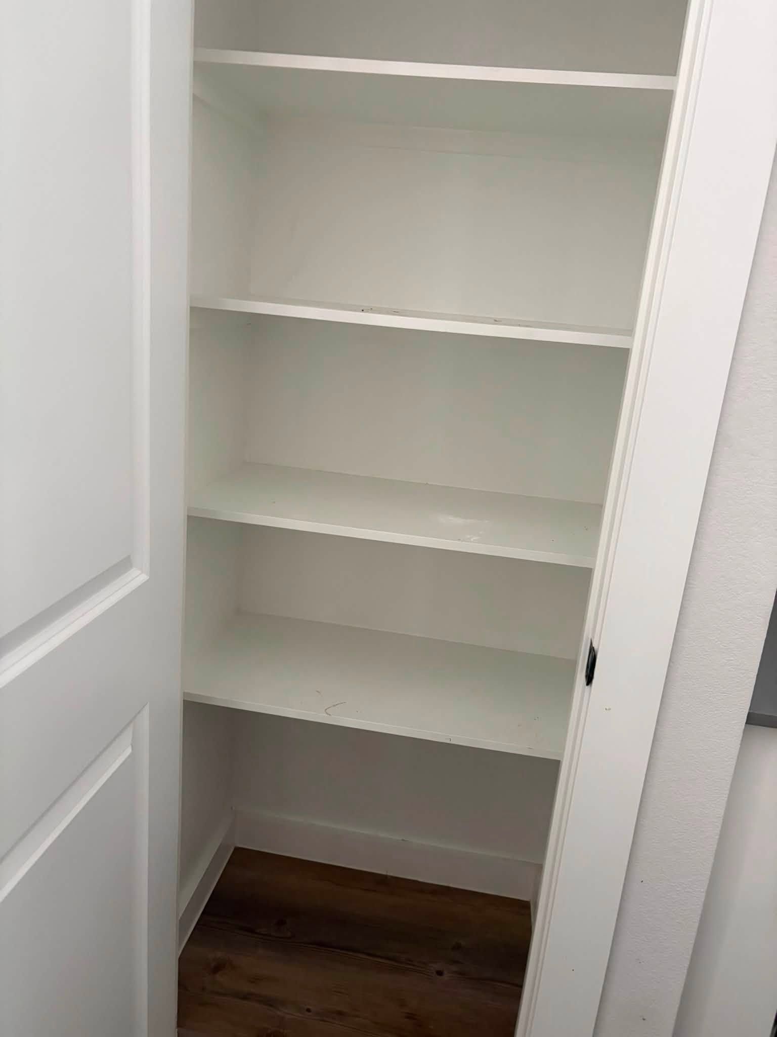 Open white closet with empty shelves and dark wood floor