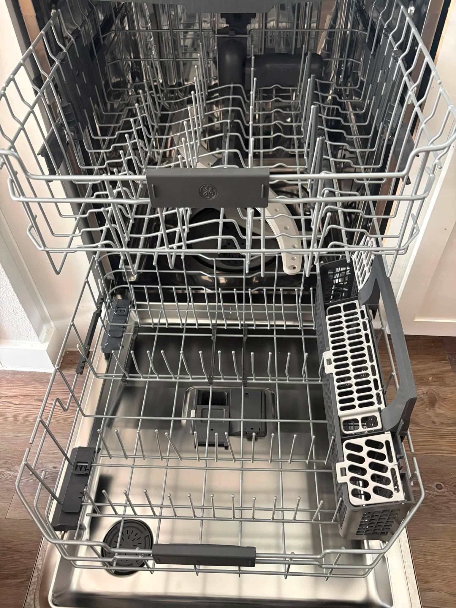 Open dishwasher with empty top and bottom racks, silverware basket, and utensil holder.