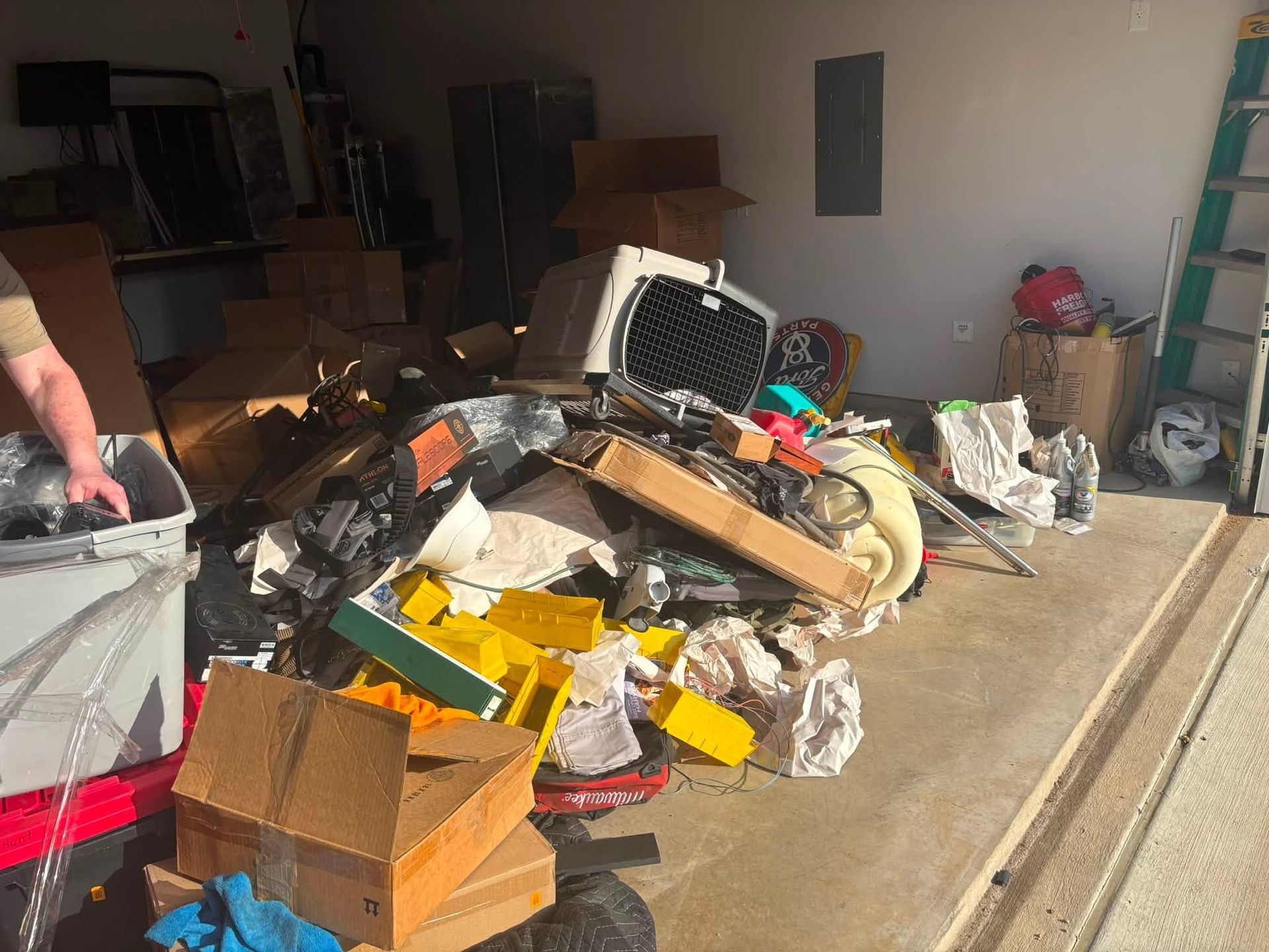 Messy garage floor piled with debris, boxes, and assorted junk near an open door