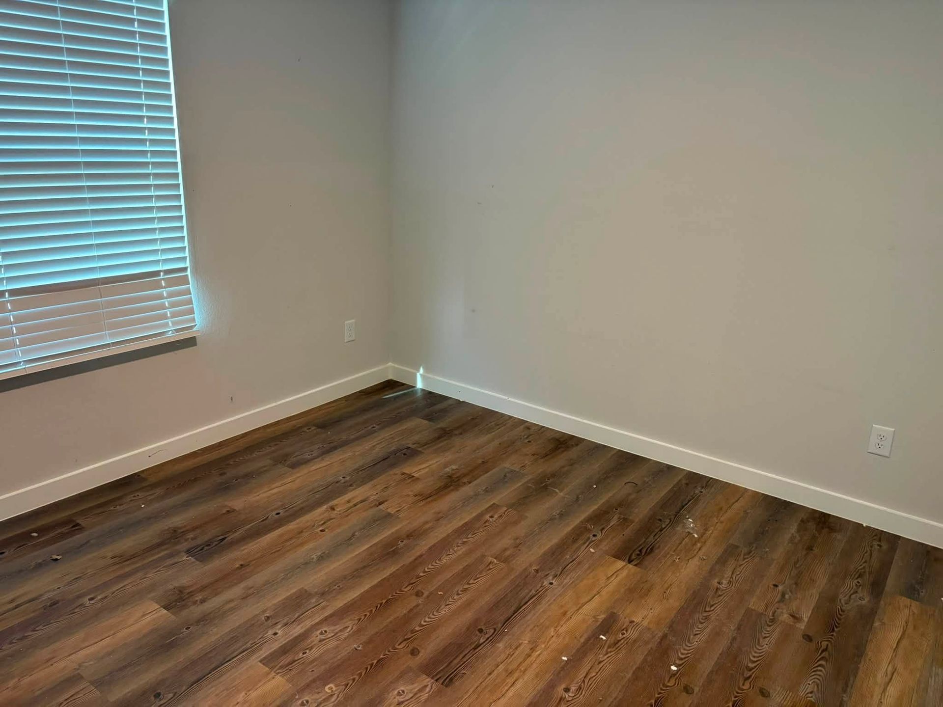 Empty room with wood-patterned floor, white walls, and a window with blinds.