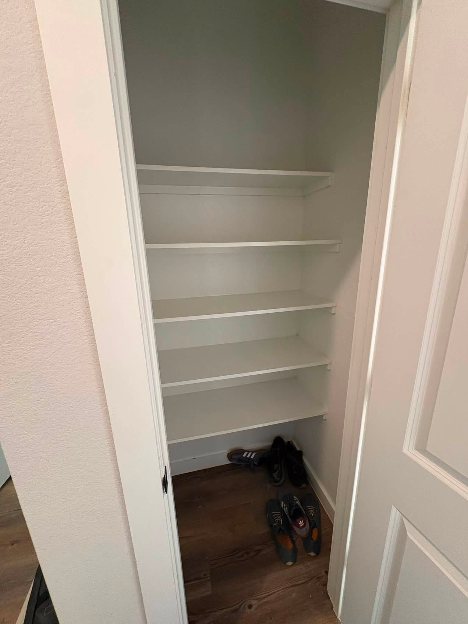 Open closet with white shelves and shoes on the floor