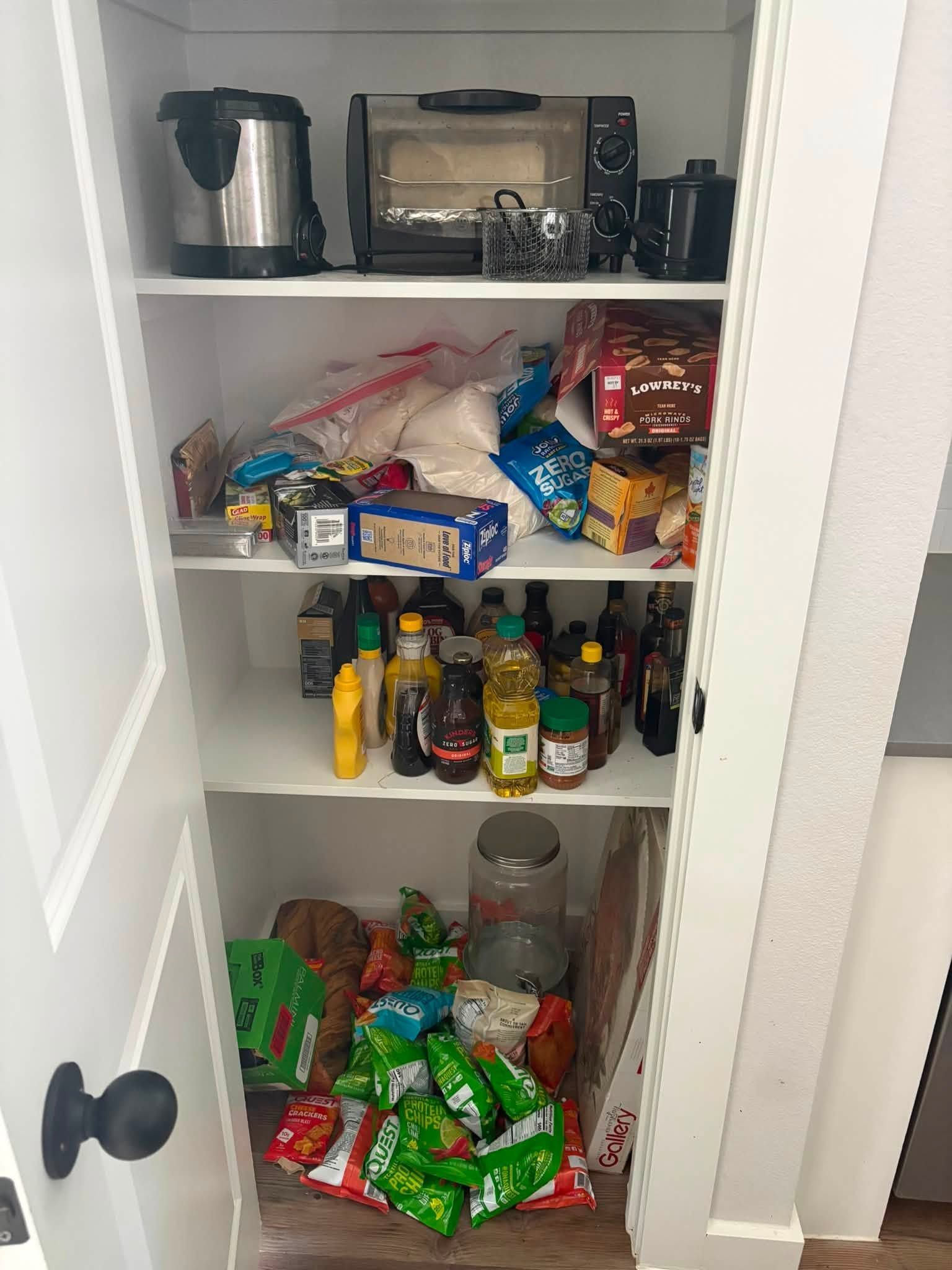 Pantry shelf packed with snacks, condiments, cereal, toaster oven, and a kettle