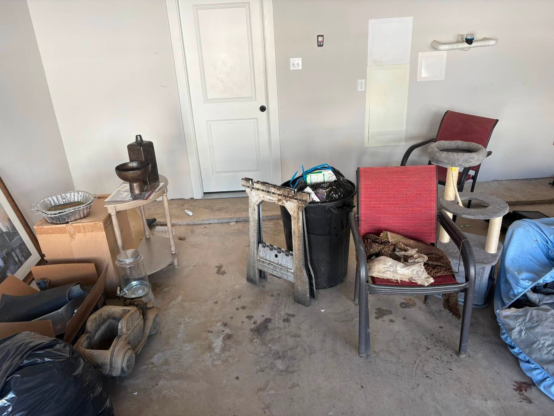 Cluttered garage with chairs, boxes, tools, and a blue tarp on the floor.