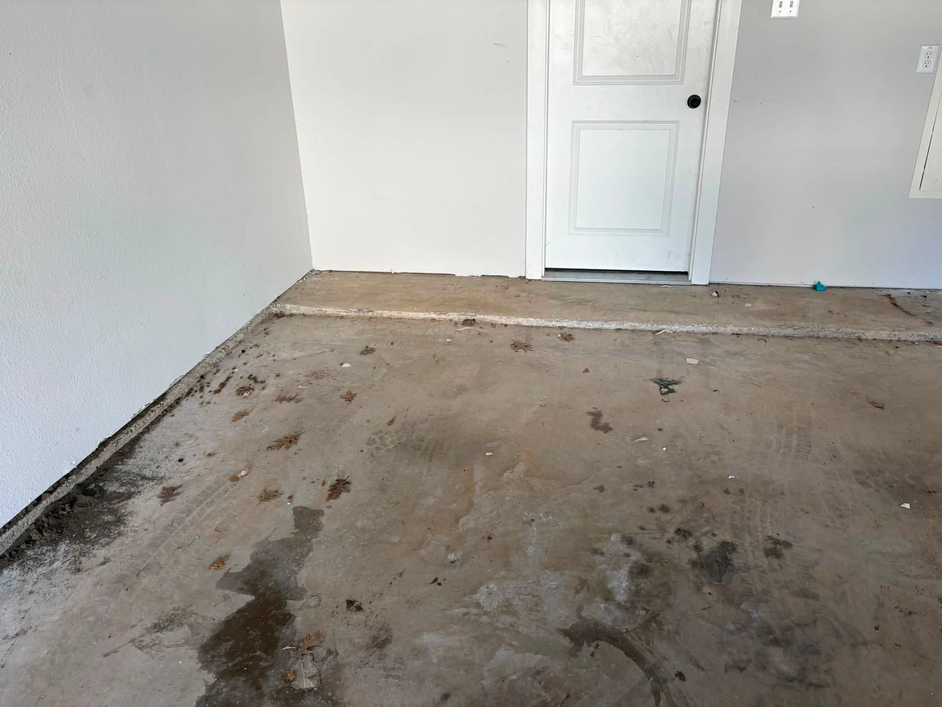 Empty room with stained concrete floor and white door, showing unfinished interior walls.