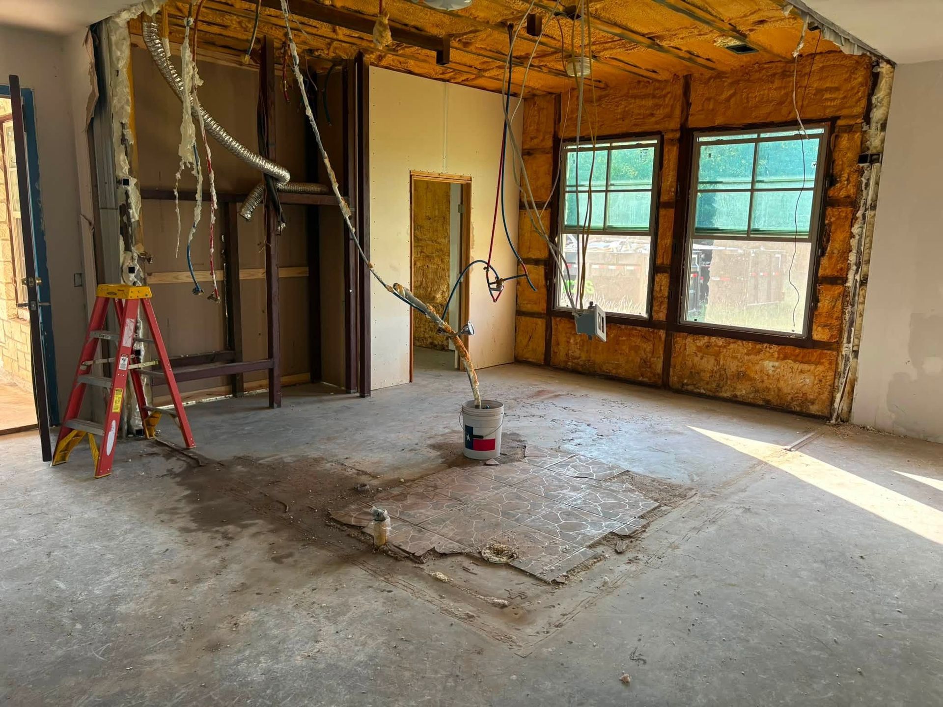Renovation site with exposed framing, ladders, and a large window letting in sunlight