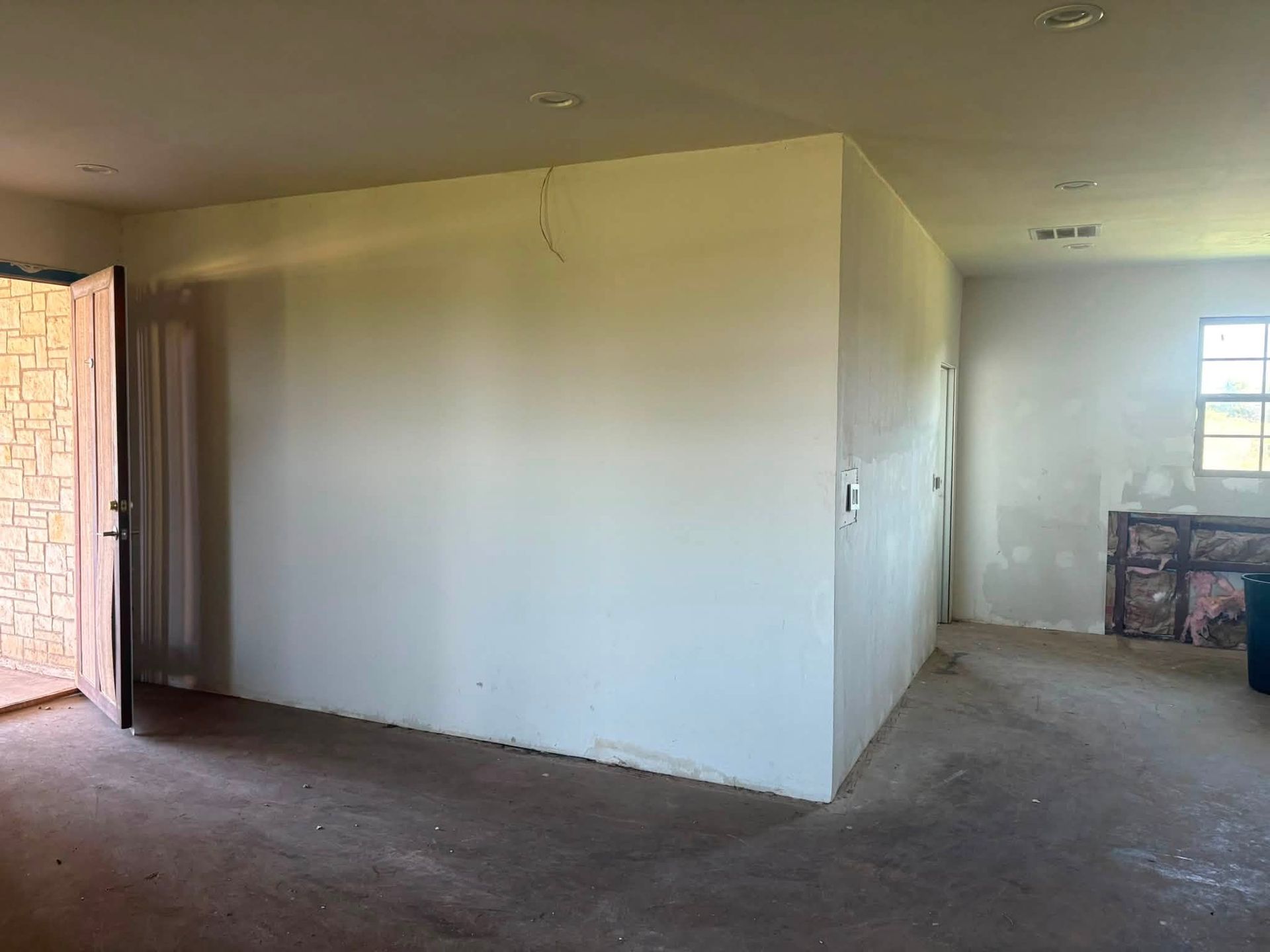 Empty unfurnished room with white walls, carpet, open door, and a window at the far end