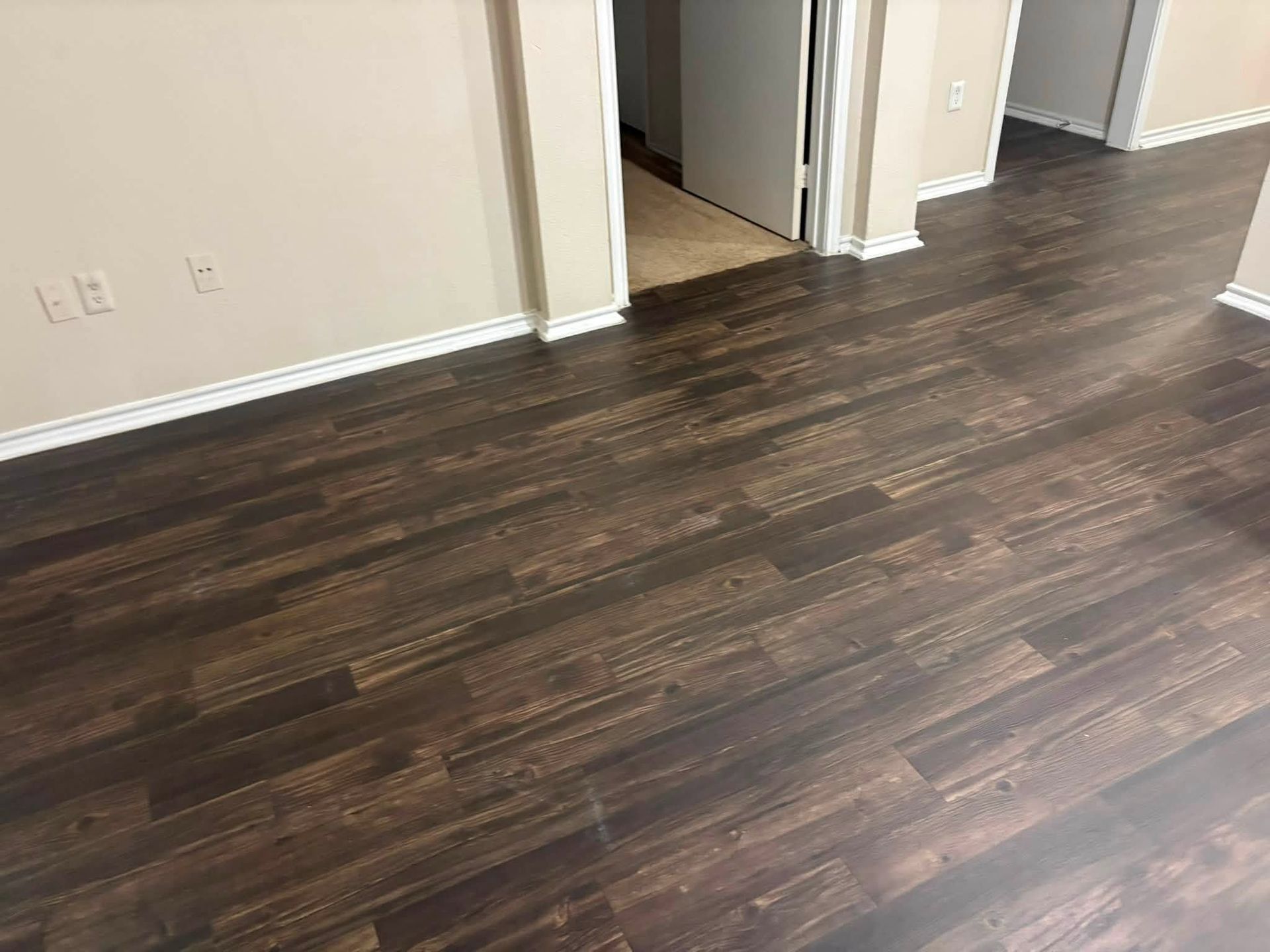 Empty room with dark wood flooring, beige walls, and open doorways to hall and adjacent room