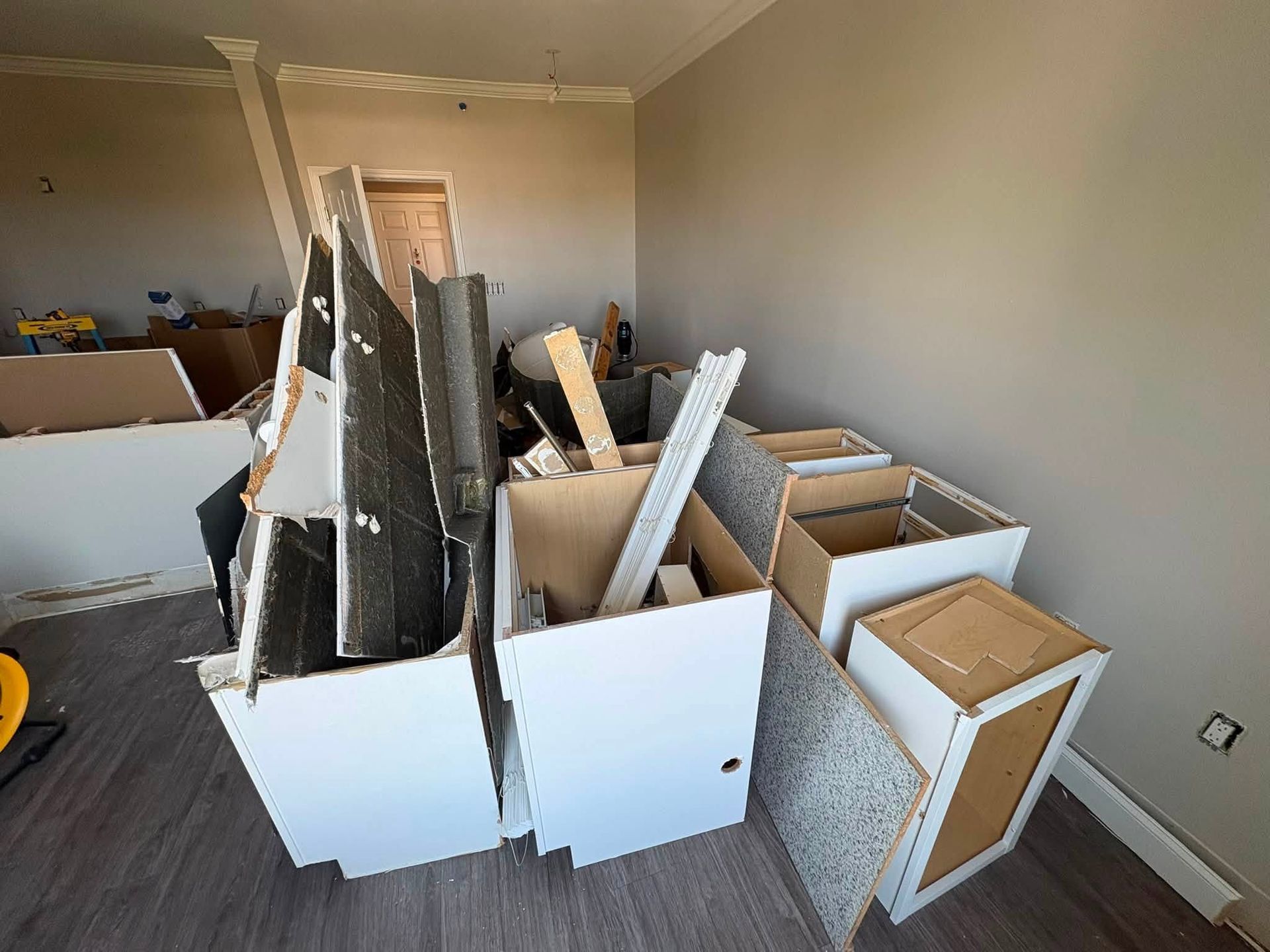 Stacked broken cabinets and wood panels clutter a room under renovation.