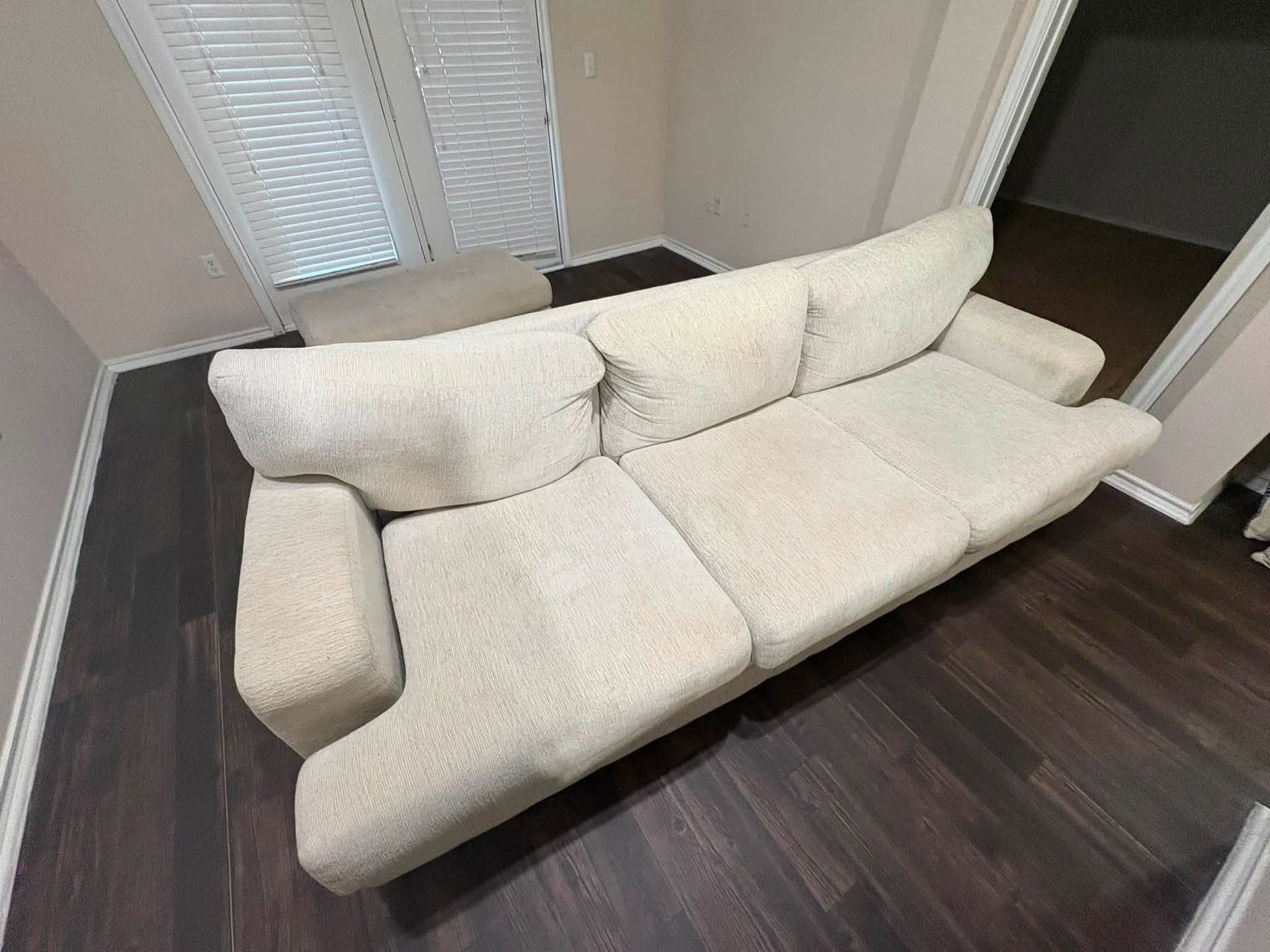 White sectional sofa in a modern room with dark wood flooring and closed blinds near a doorway.