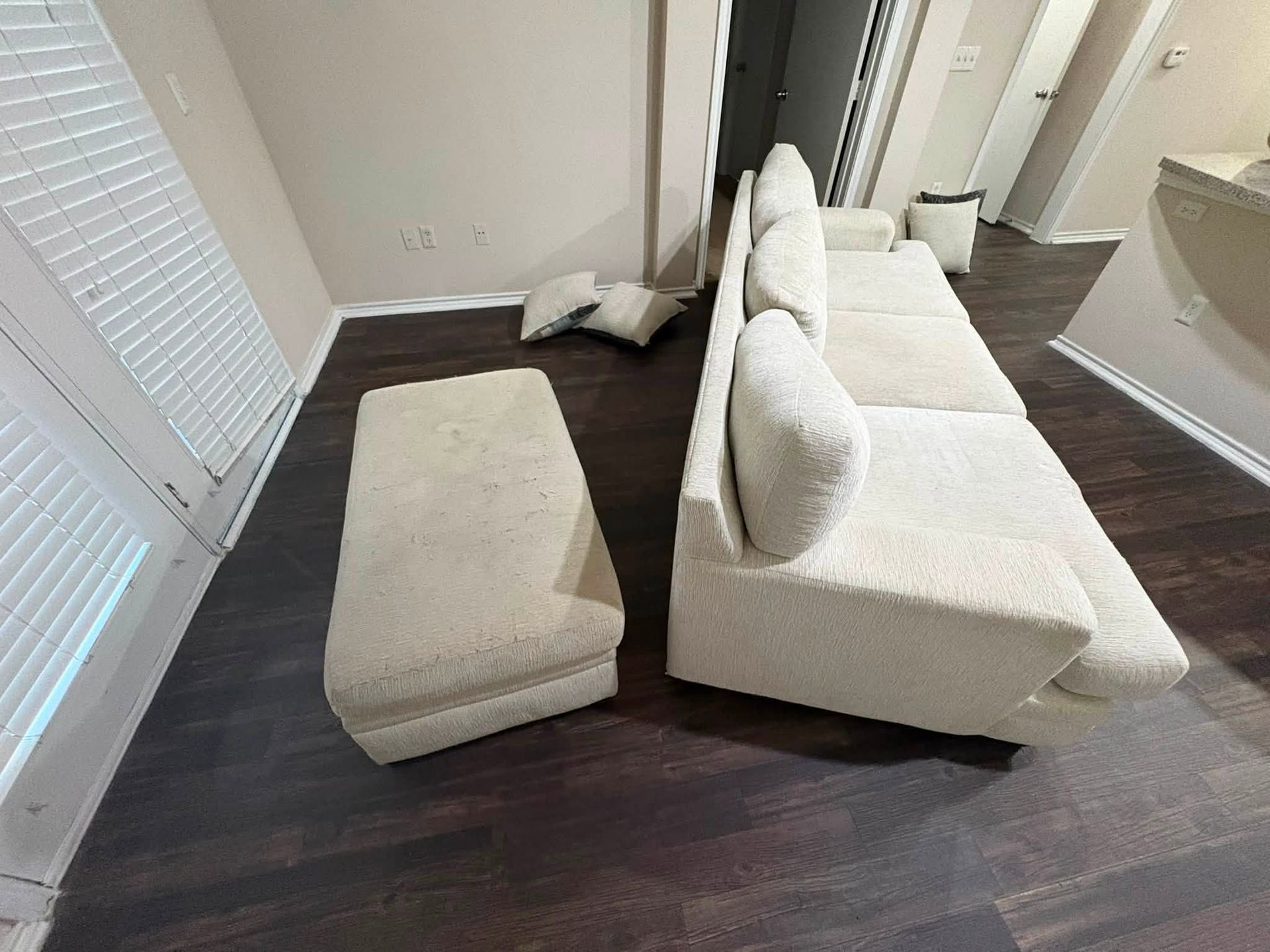 Light beige sectional sofa with matching ottoman in a bright room with dark wood floors