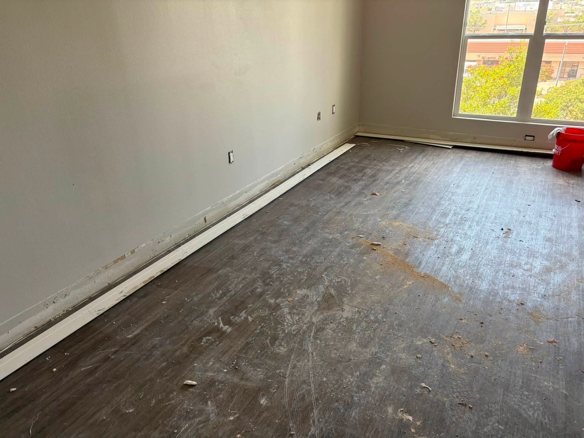 Empty room with bare walls, worn flooring, and a window letting in daylight