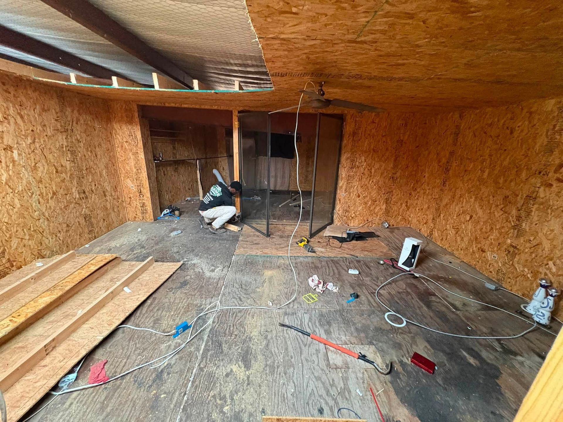 Wood-paneled attic with exposed beams, scattered tools, and plywood sheets on the floor