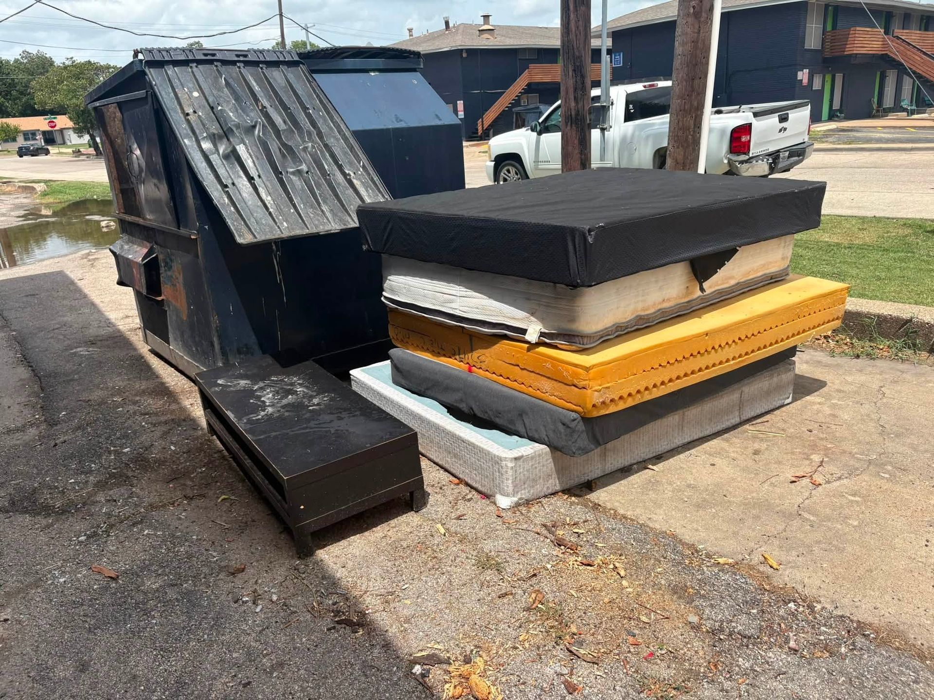 Stack of discarded mattresses and bed frames on a curbside near a street.