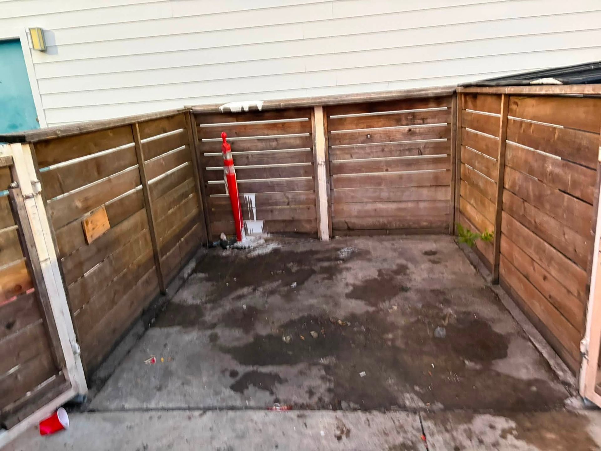 Empty fenced concrete yard with wooden privacy walls and a red post in the corner