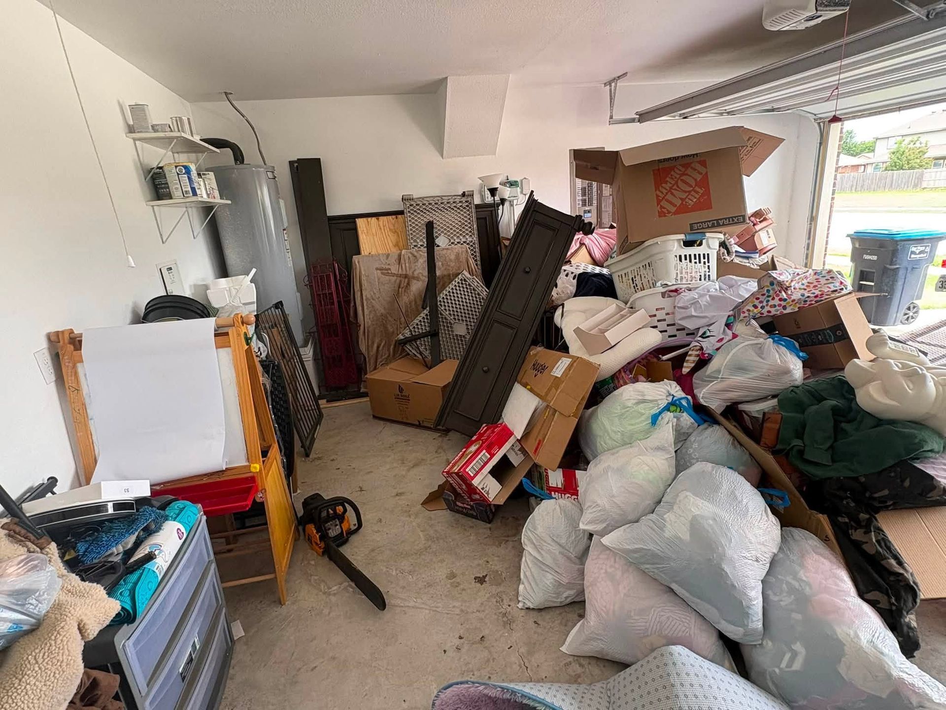 Cluttered garage with stacked boxes, bags, and assorted items piled across the floor and shelves.