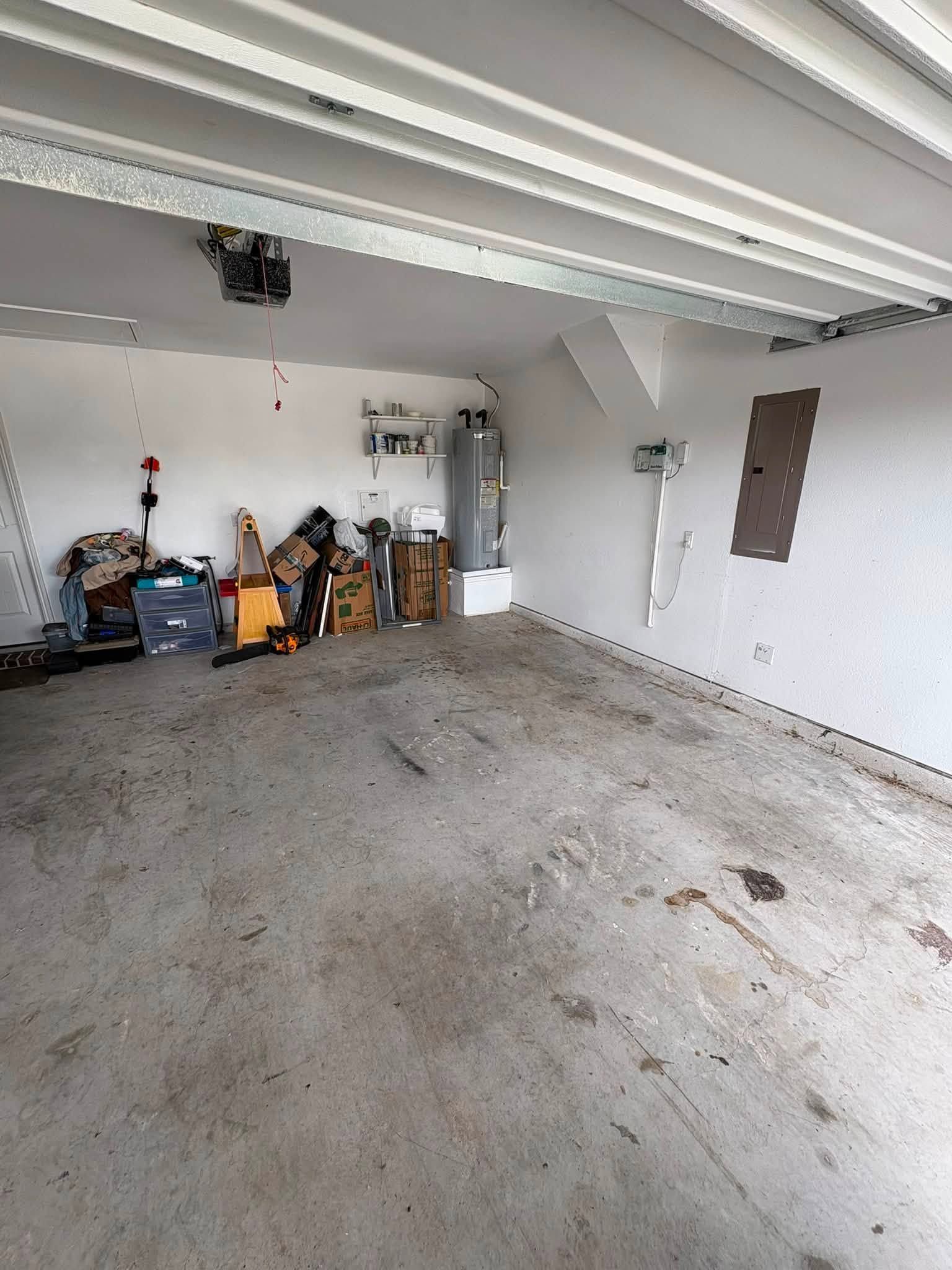 Empty garage interior with concrete floor, white walls, exposed ceiling beams, and stored tools in back left.