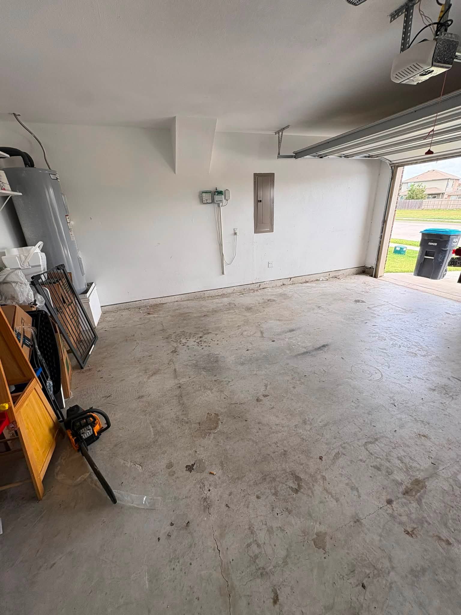 Empty garage with concrete floor, white walls, and an open door letting in daylight.