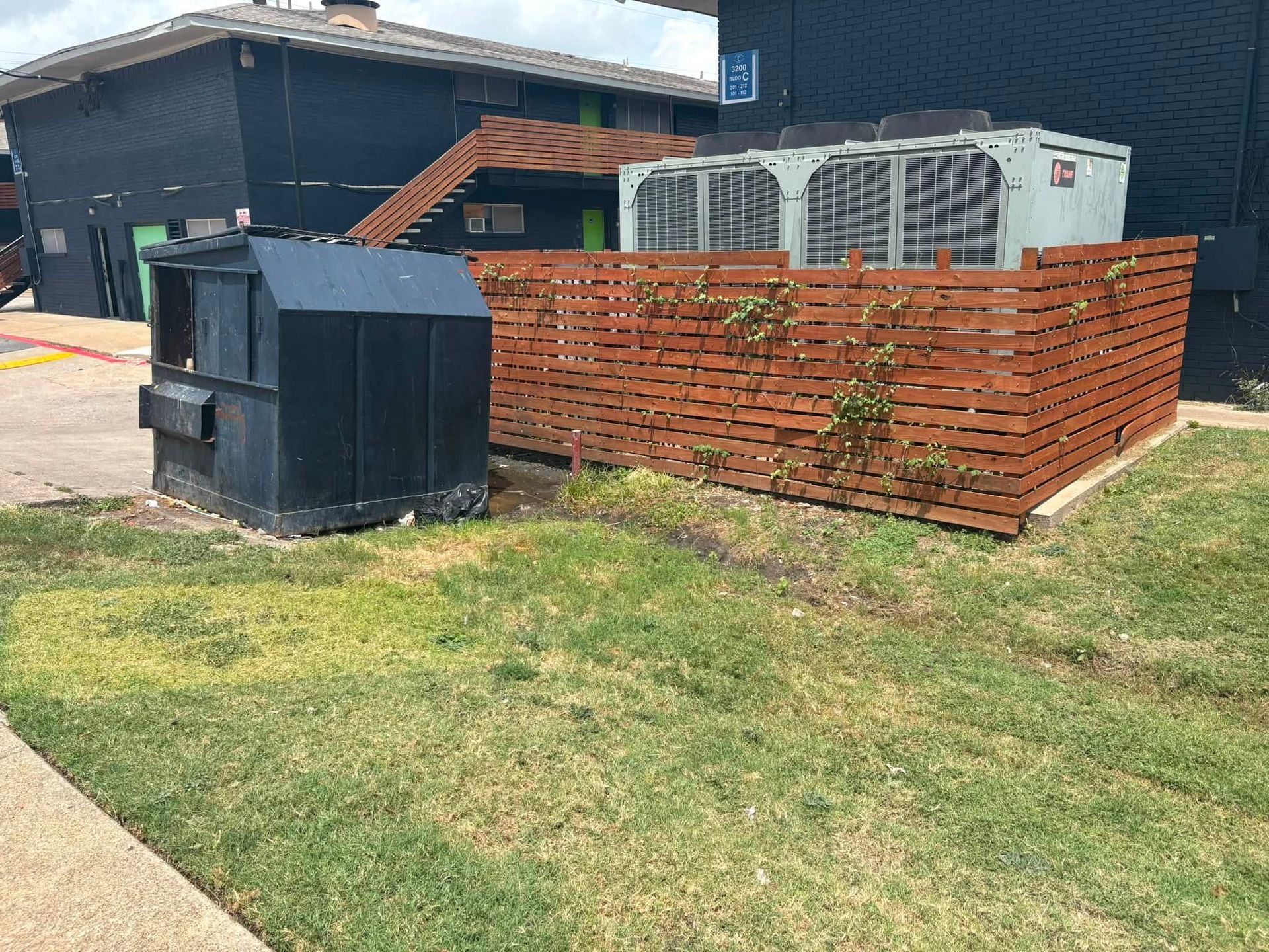 Residential backyard with black utility bins, red brick fence, and green grass beside a house