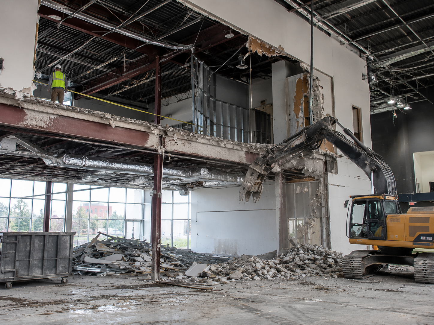 Interior demolition of a damaged building, with rubble, exposed beams, and an excavator on the right.