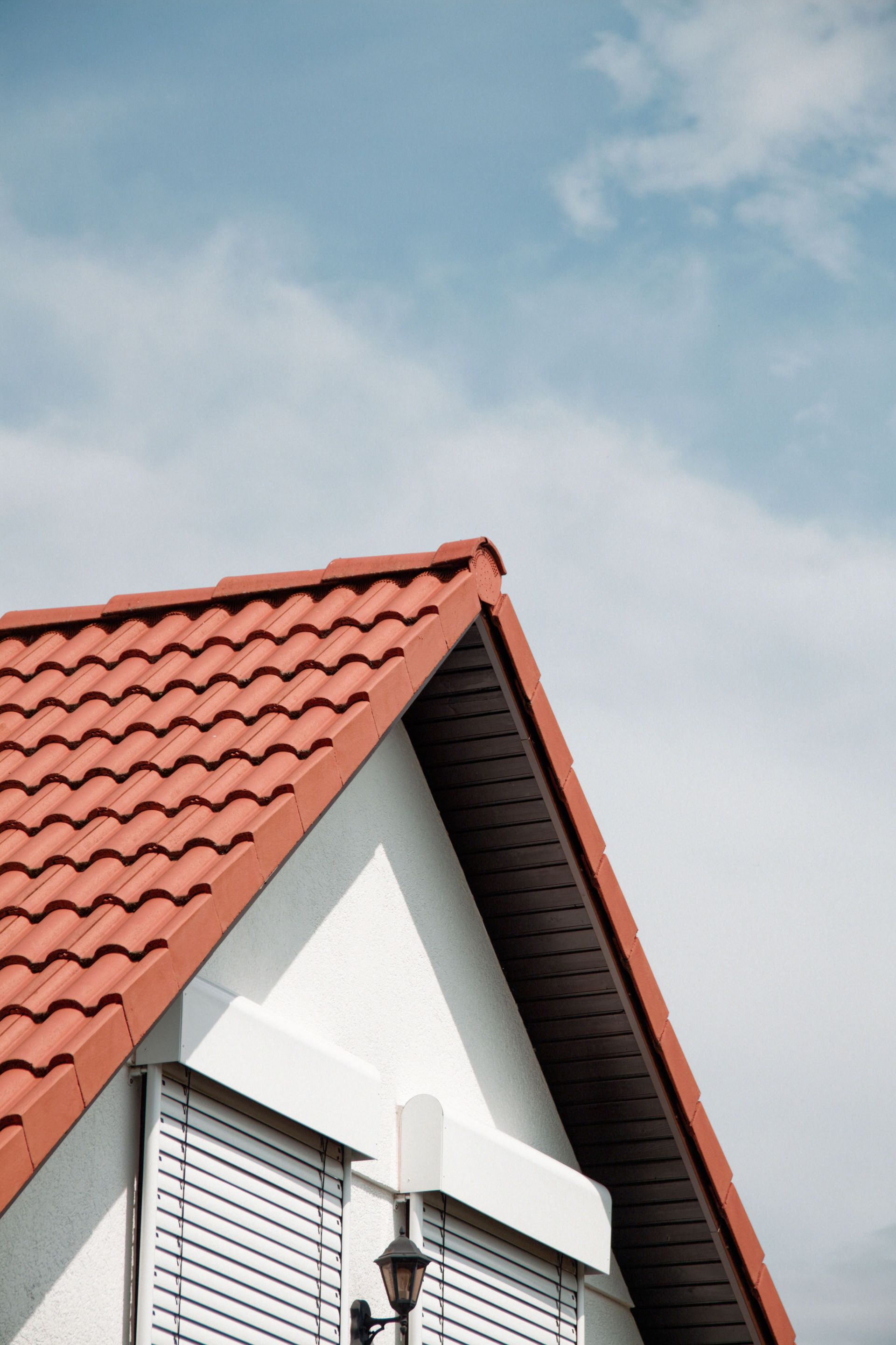 Red tiled house roof with white gable under a blue, cloudy sky
