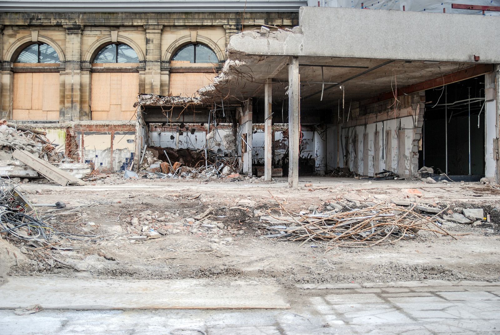 Collapsed building interior with rubble, exposed columns, and arched windows amid heavy damage