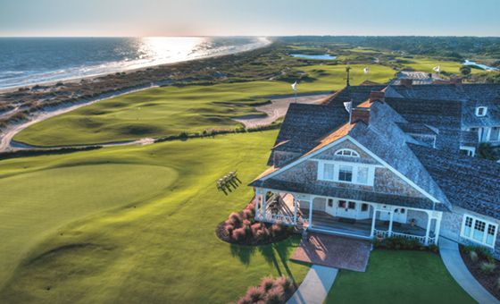 Aerial view of a seaside golf course beside a large coastal clubhouse at sunset