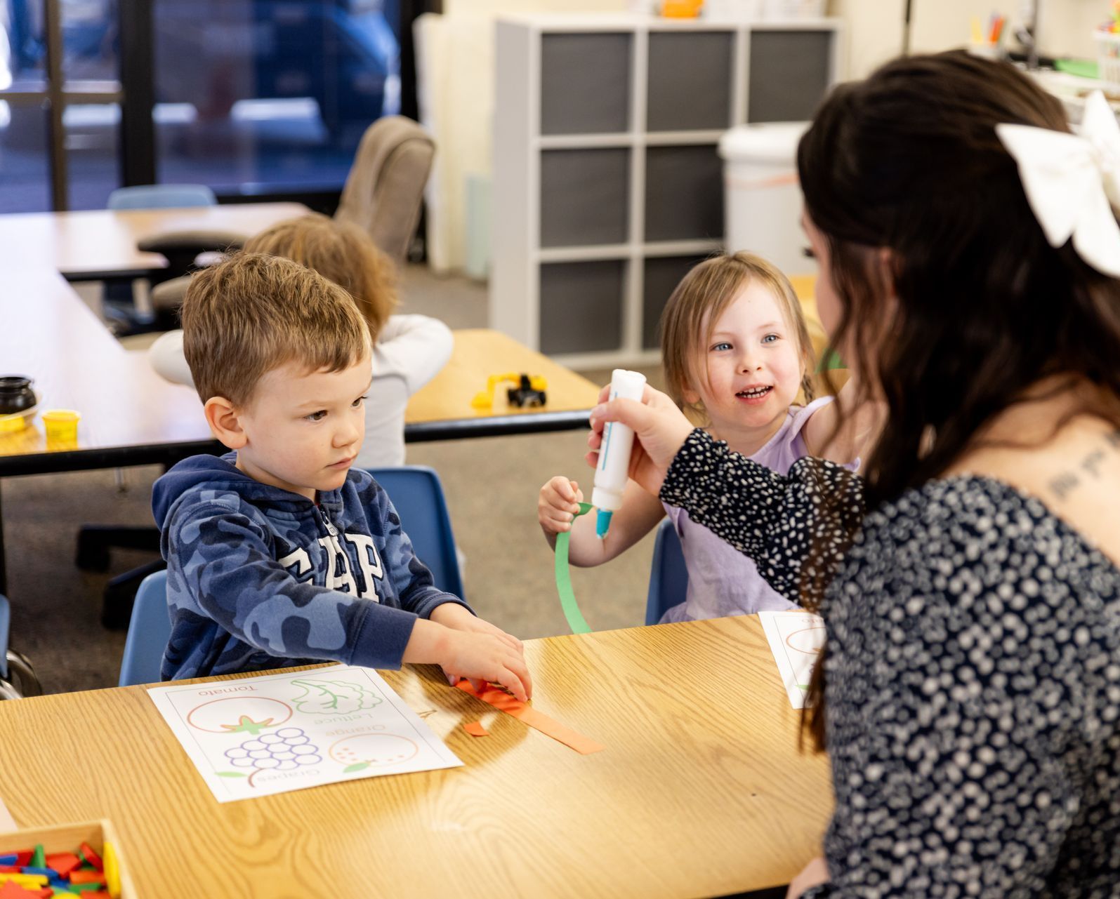 Teacher helping two children with a classroom activity at a wooden table