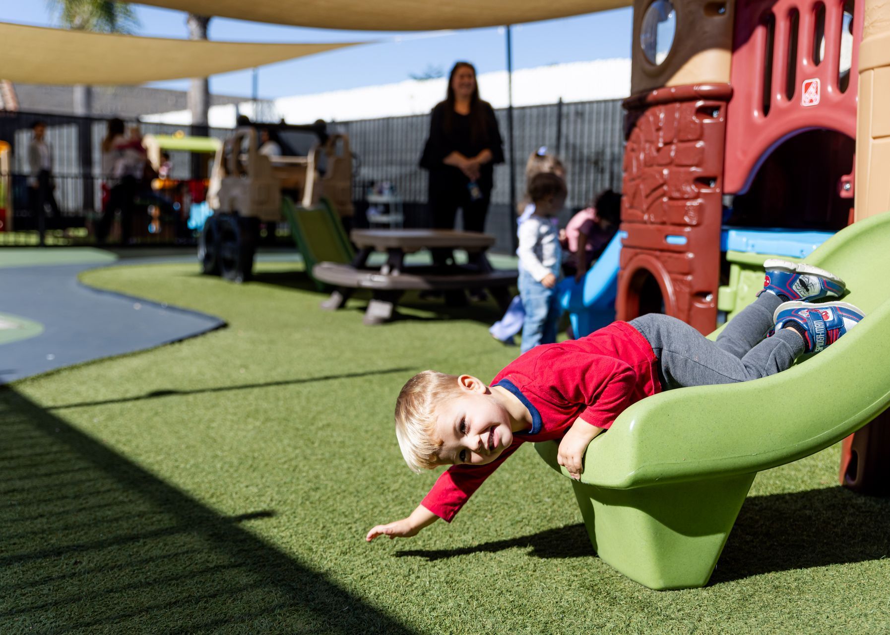 Child in a red shirt sliding headfirst on a green playground slide under a canopy
