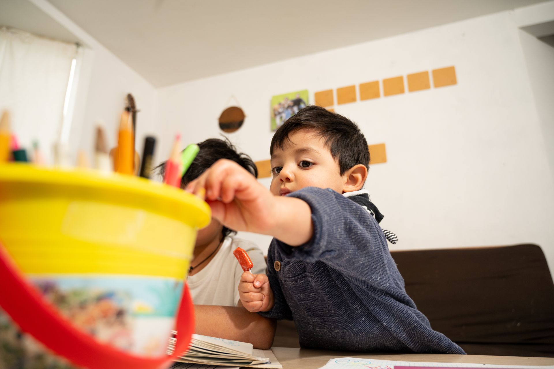 Child reaching across a table toward a colorful bowl in a bright room