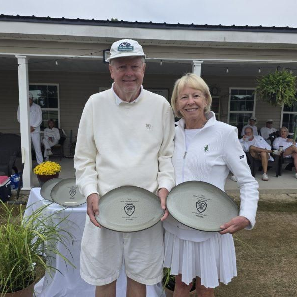 Two people holding plates outdoors. Both wearing white clothing. One person is male, one is female.