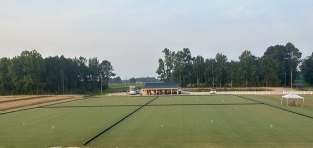 Green grass field with a building and trees in the background. A white tent is on the right side.