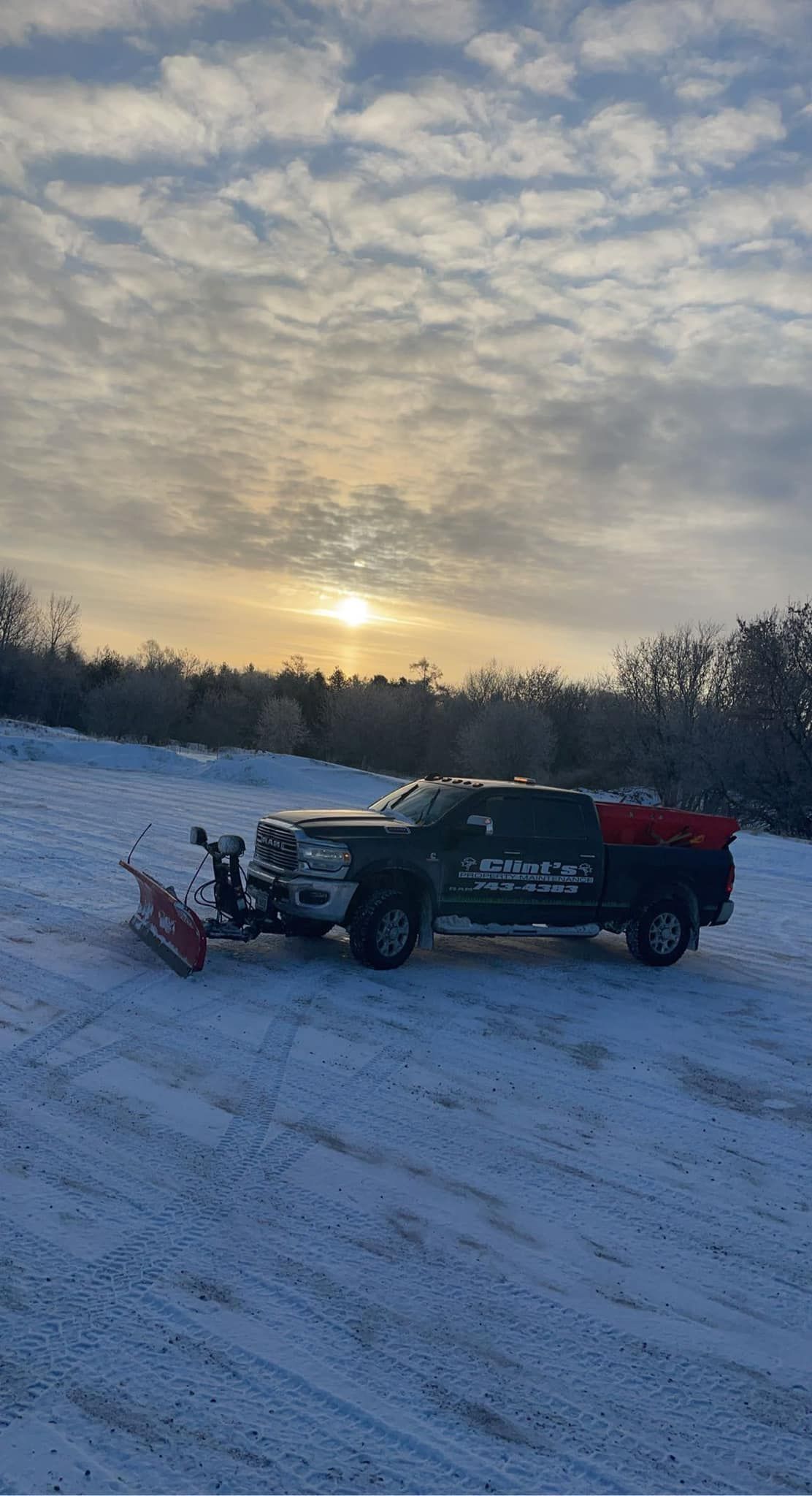 A snow plow is parked in the snow in a parking lot.
