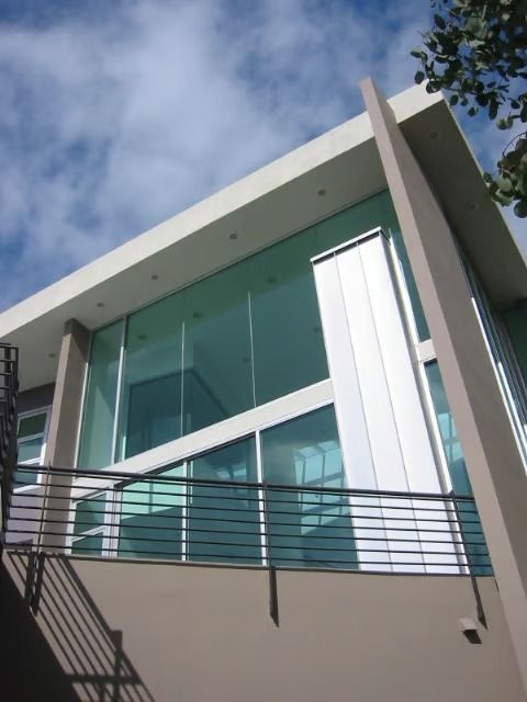 A low-angle view of a modern building with large glass windows, a white roof overhang, and a metal railing.