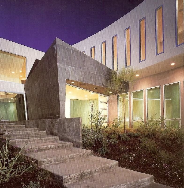 A modern building at twilight, featuring a stone-clad entrance, wide stone steps, and a row of vertical rectangular windows.