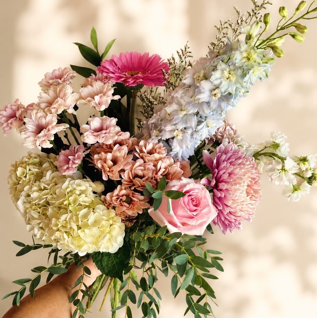 Bouquet à main composé de fleurs roses, pêche, blanches et lavande avec du feuillage vert