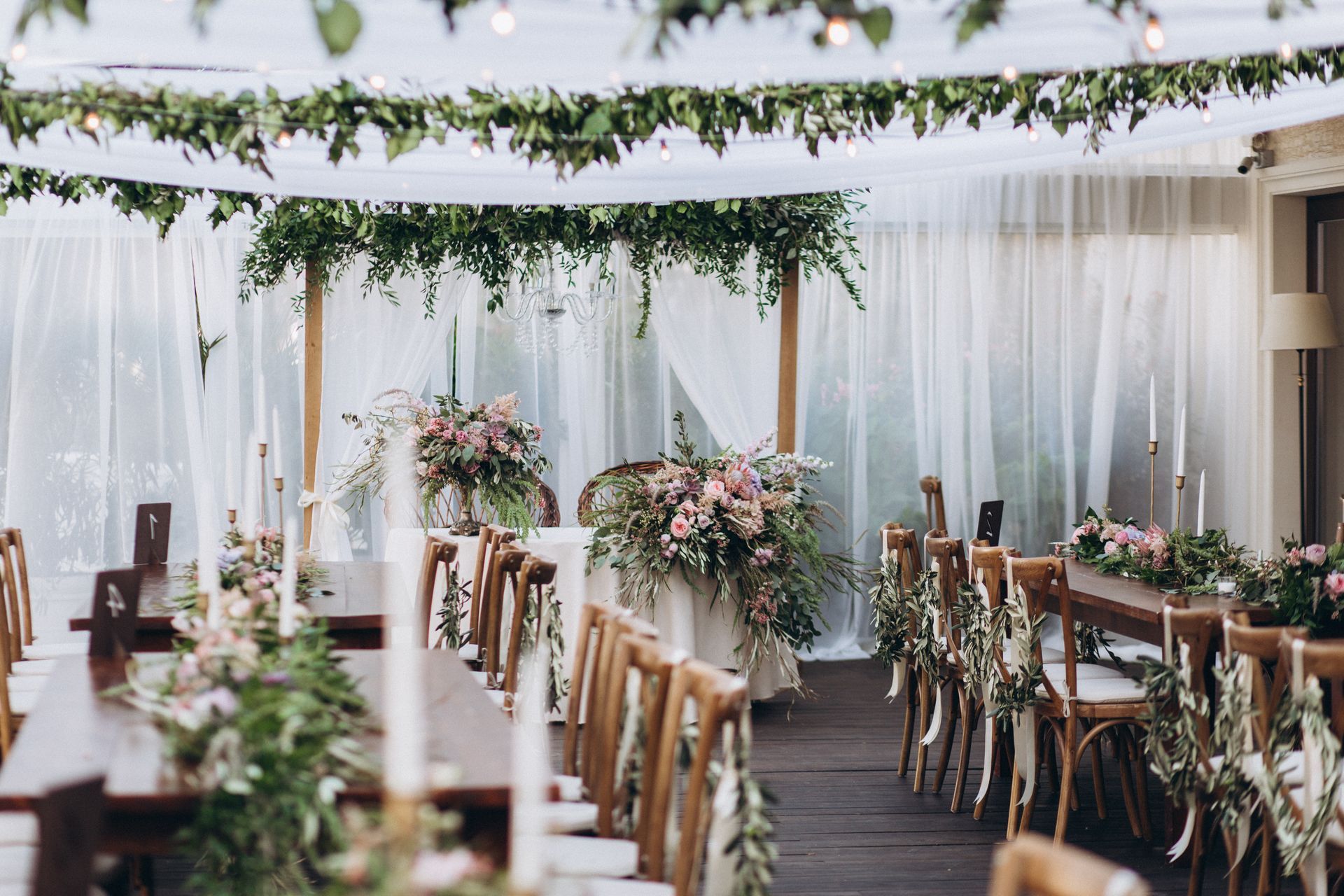 Réception de mariage élégante en plein air avec des tentures blanches, des compositions florales et des chaises en bois sous un écrin de verdure.