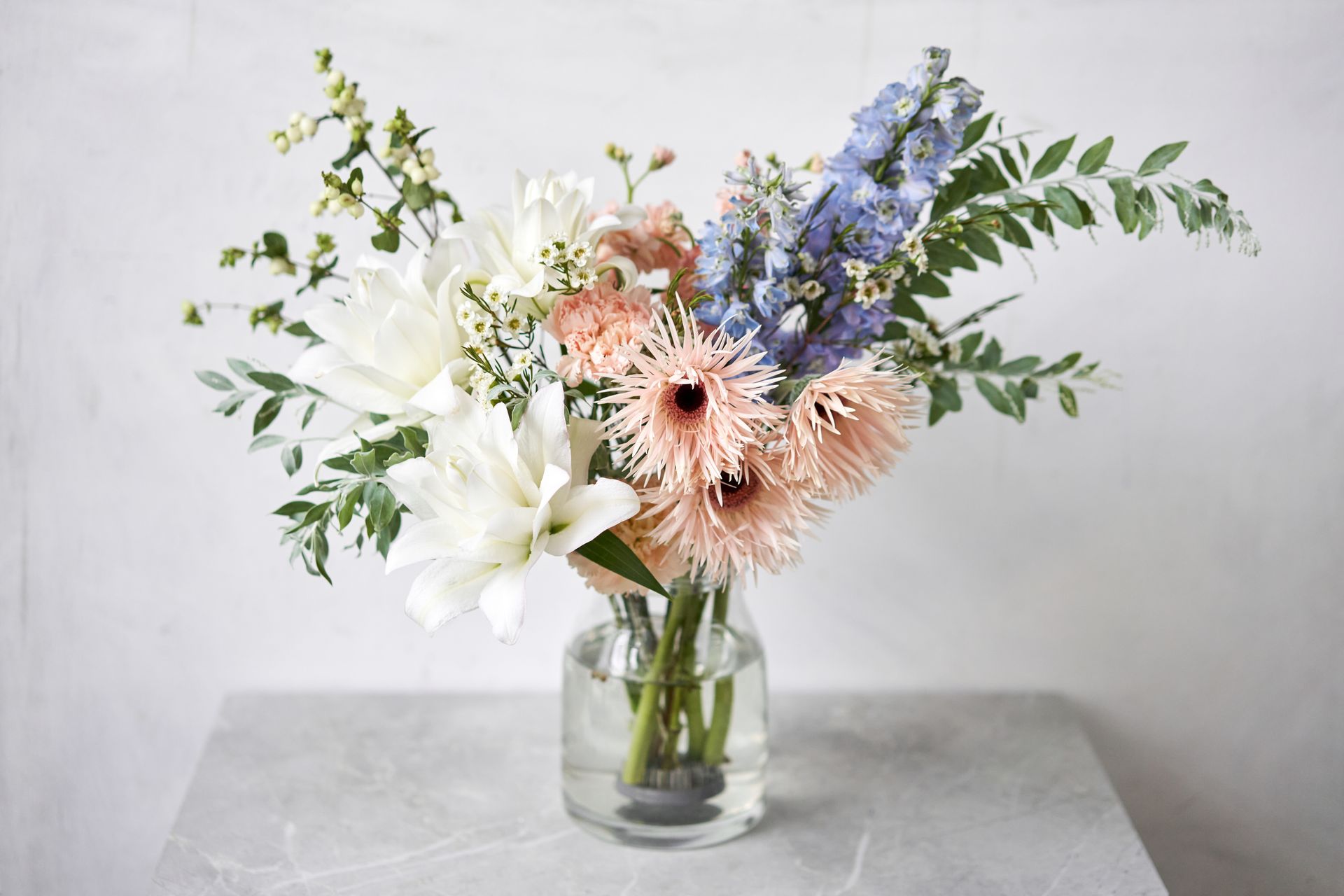 Bouquet mixte de fleurs blanches, pêche et bleues dans un vase en verre transparent sur une table grise