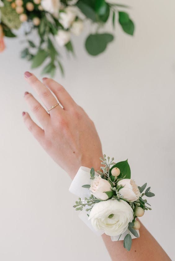 Main avec un corsage de poignet et une bague à fleurs blanches sur un fond vert tendre