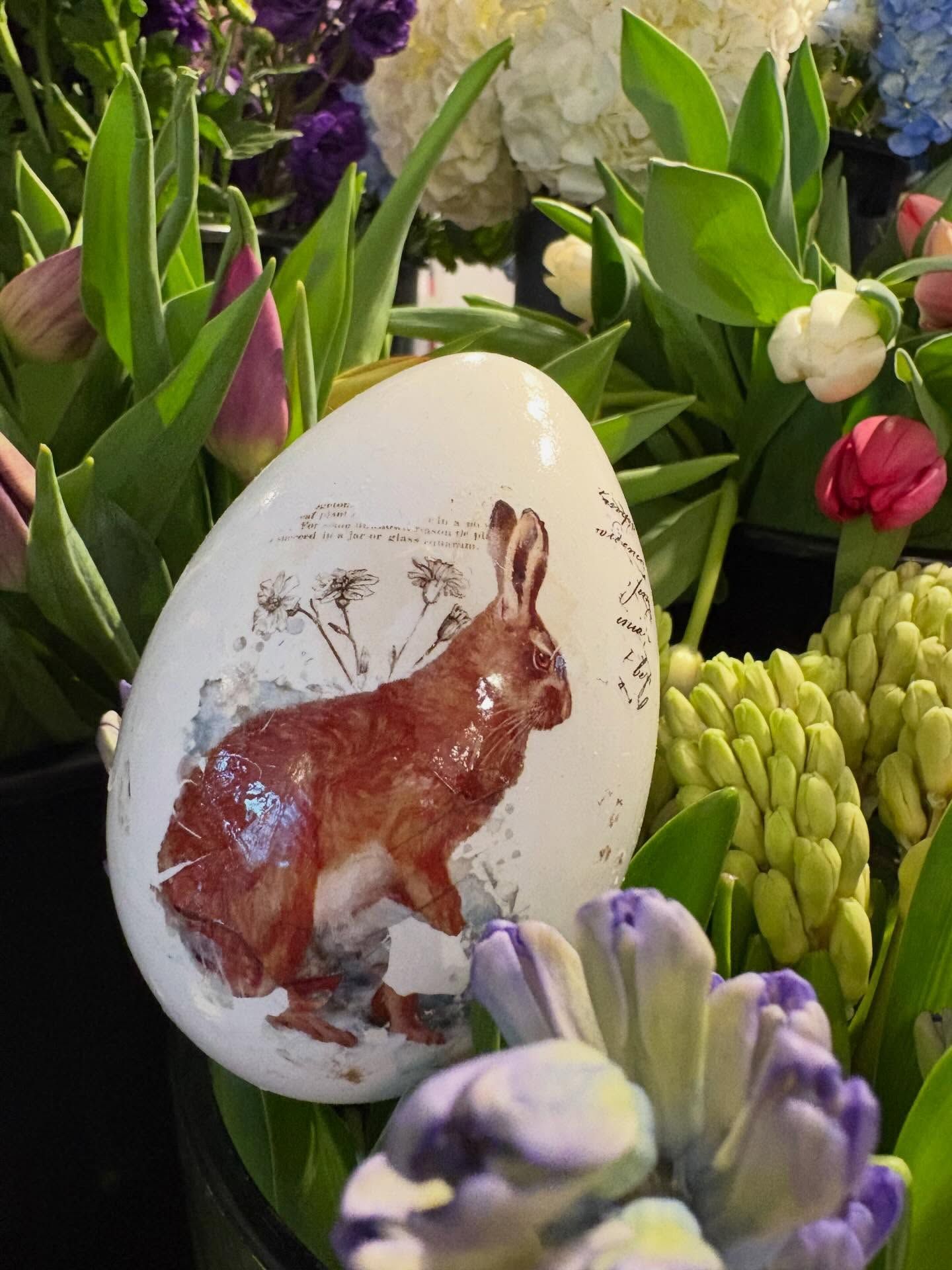 Œuf blanc décoratif orné d'un lapin brun parmi des fleurs violettes, vertes et blanches