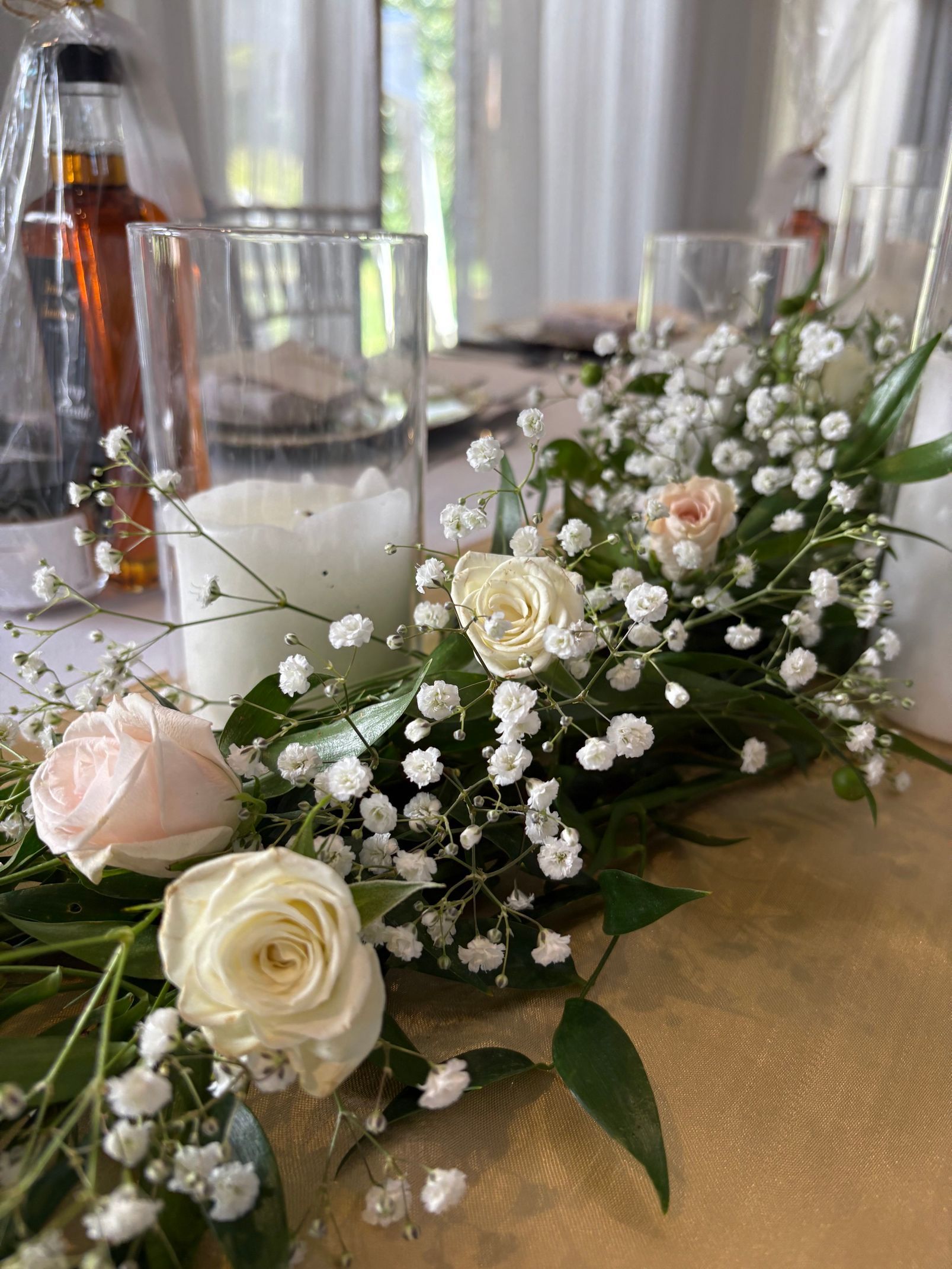 Composition florale de roses blanches et de gypsophile sur une table avec de la verrerie et des bouteilles lors d'une célébration