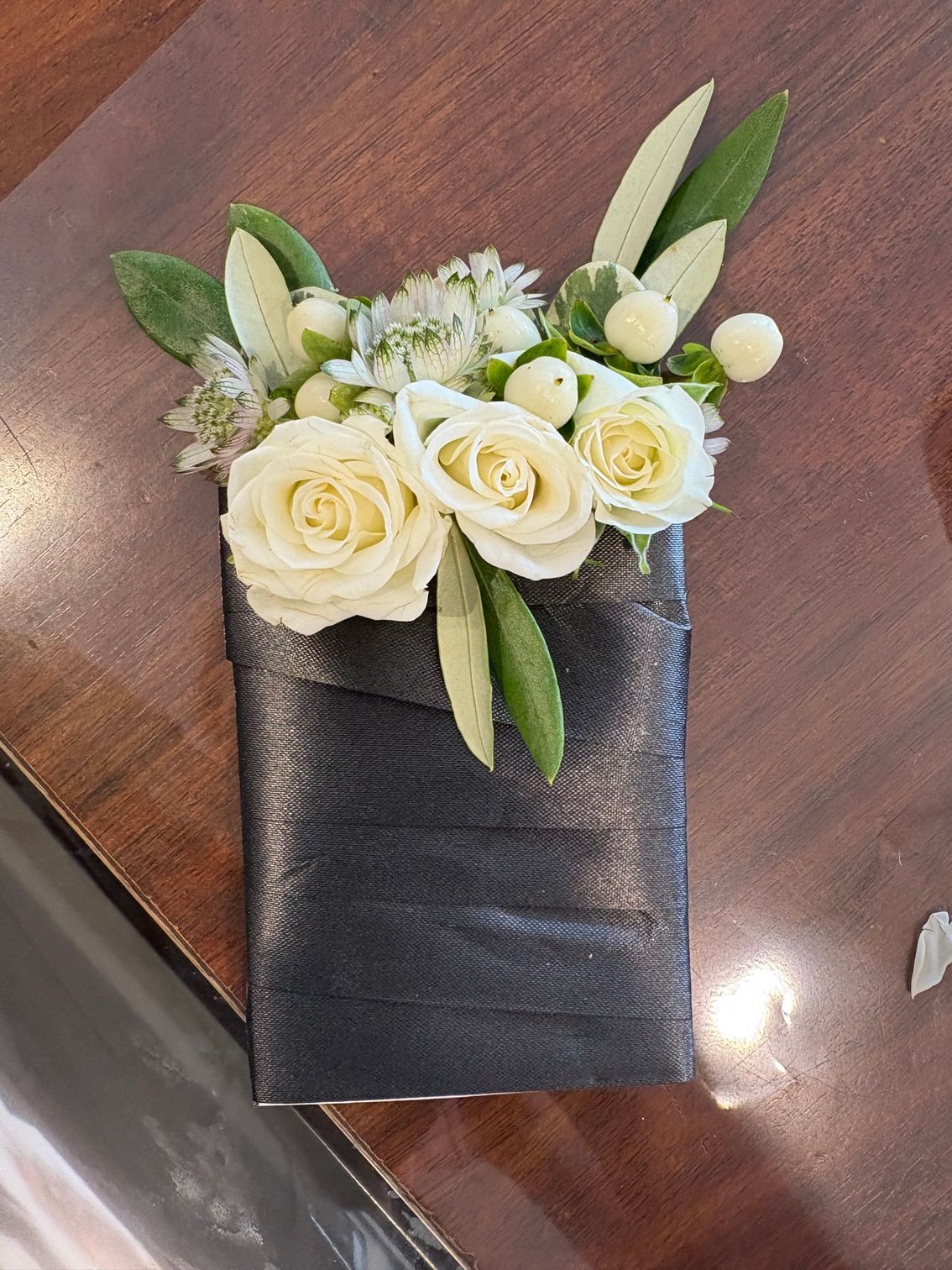 Corsage de rose blanche avec feuillage sur un ruban noir, posé sur une surface en bois