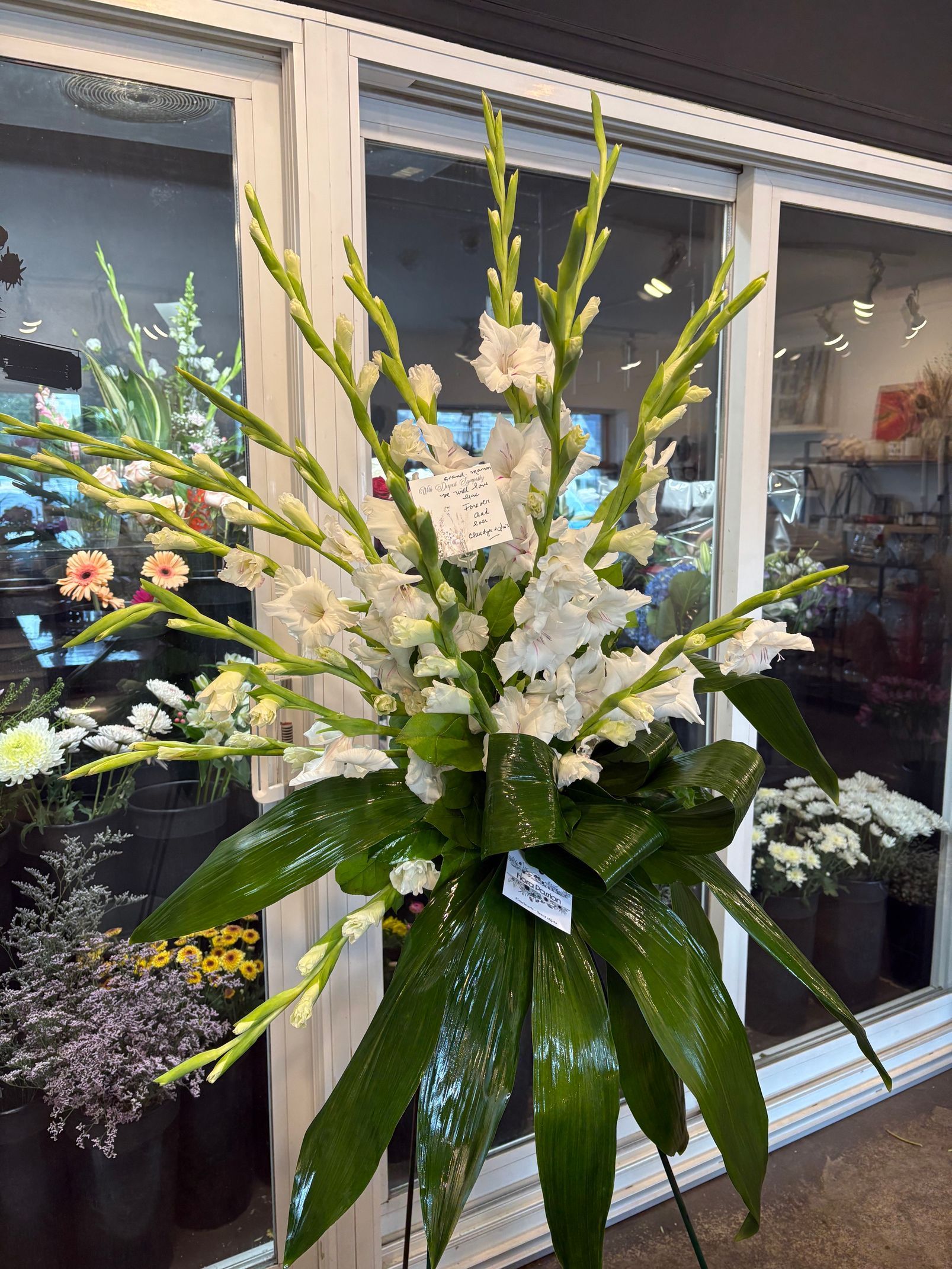 Grand arrangement floral blanc aux feuilles vertes exposé devant une vitrine.