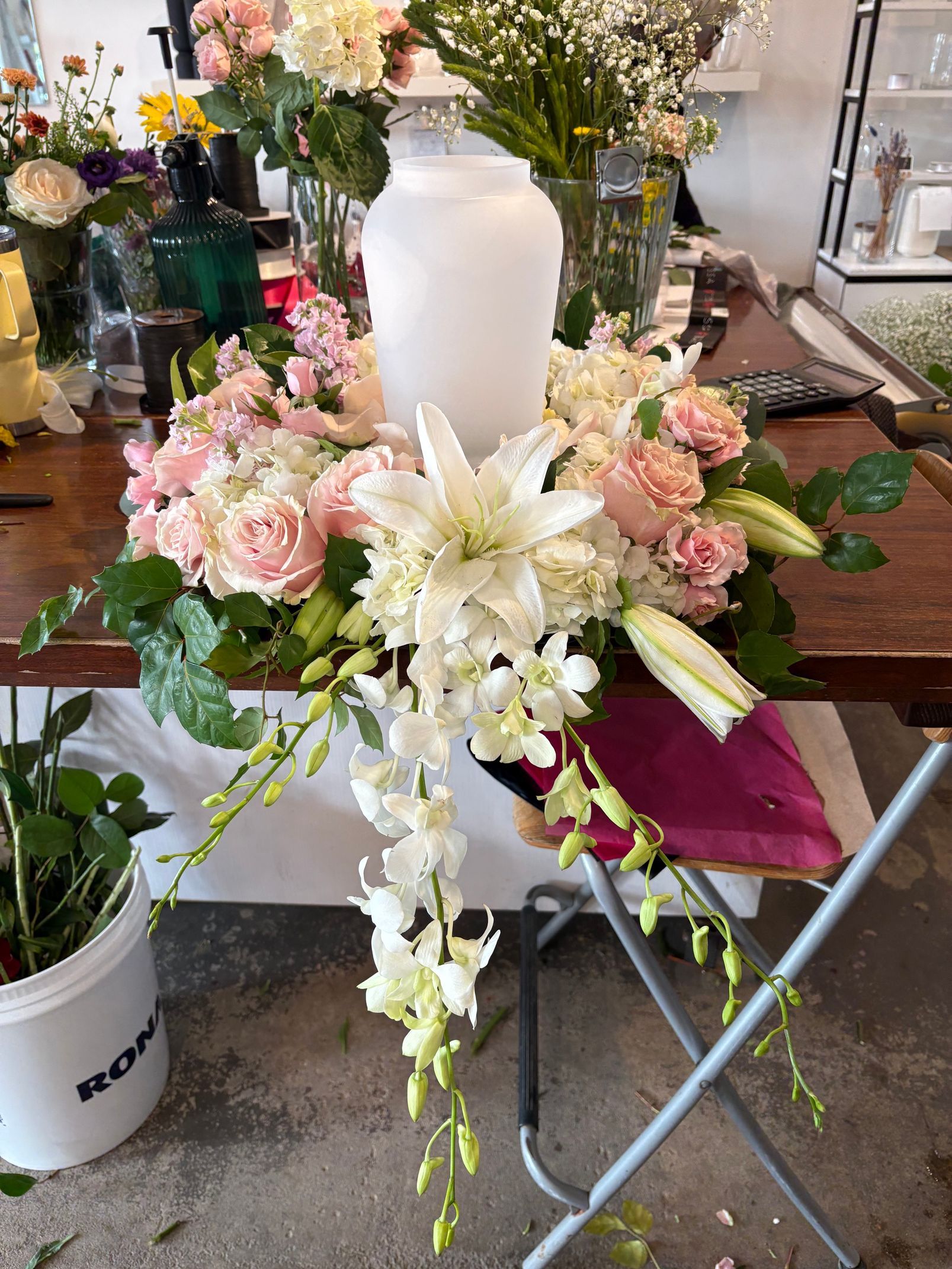 Composition florale de fleurs roses et blanches autour d'un vase blanc sur une table pliante dans un magasin.