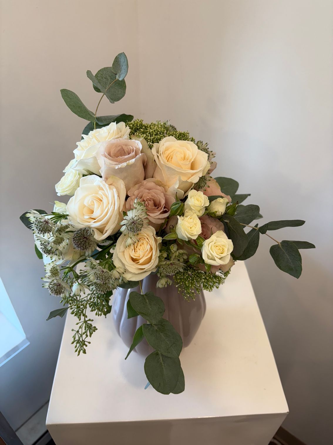 Bouquet de roses crème et rose pâle avec de la verdure dans un vase blanc sur un piédestal