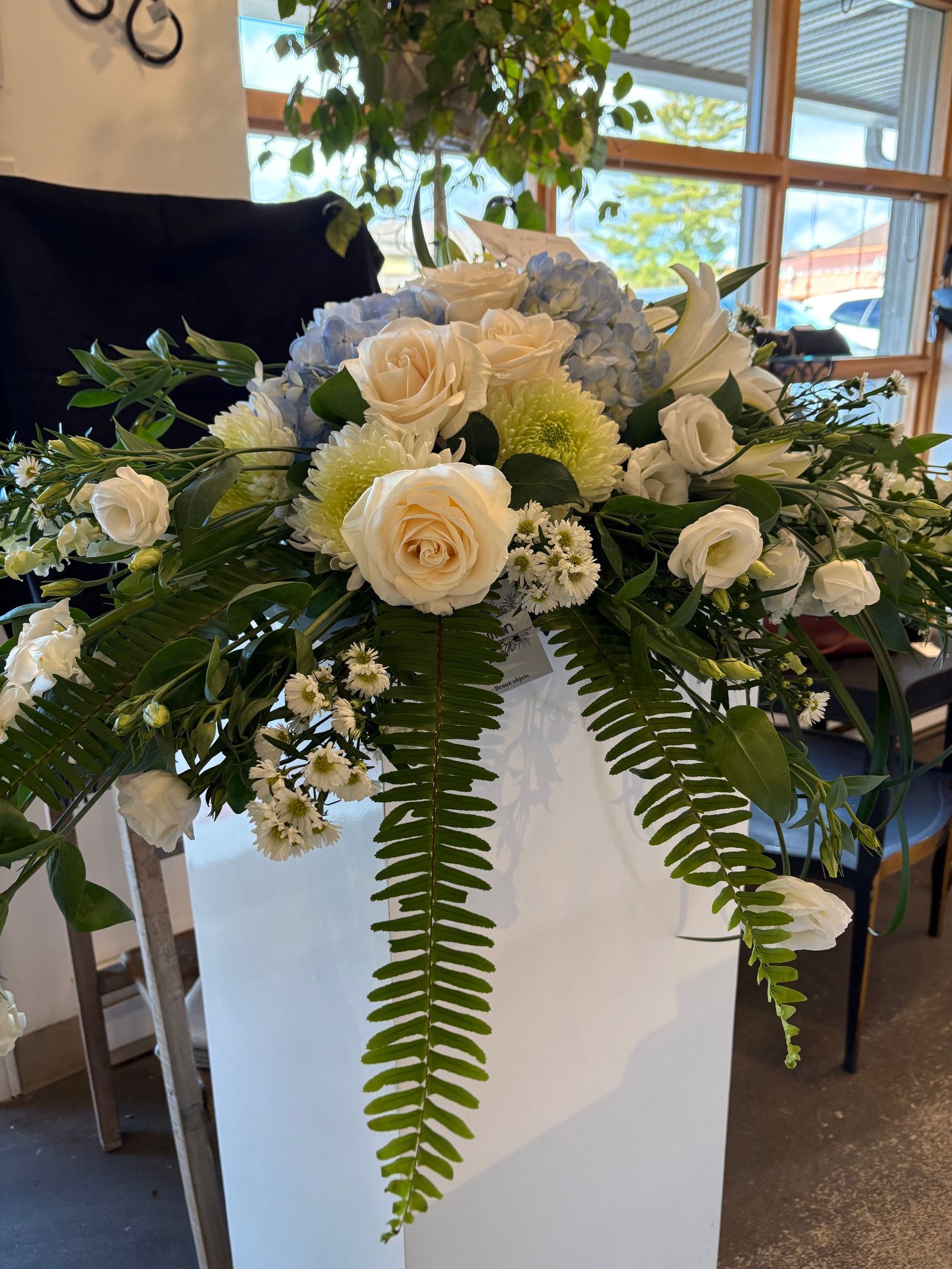 Composition florale blanche avec roses et fougères dans un grand pot blanc à l'intérieur