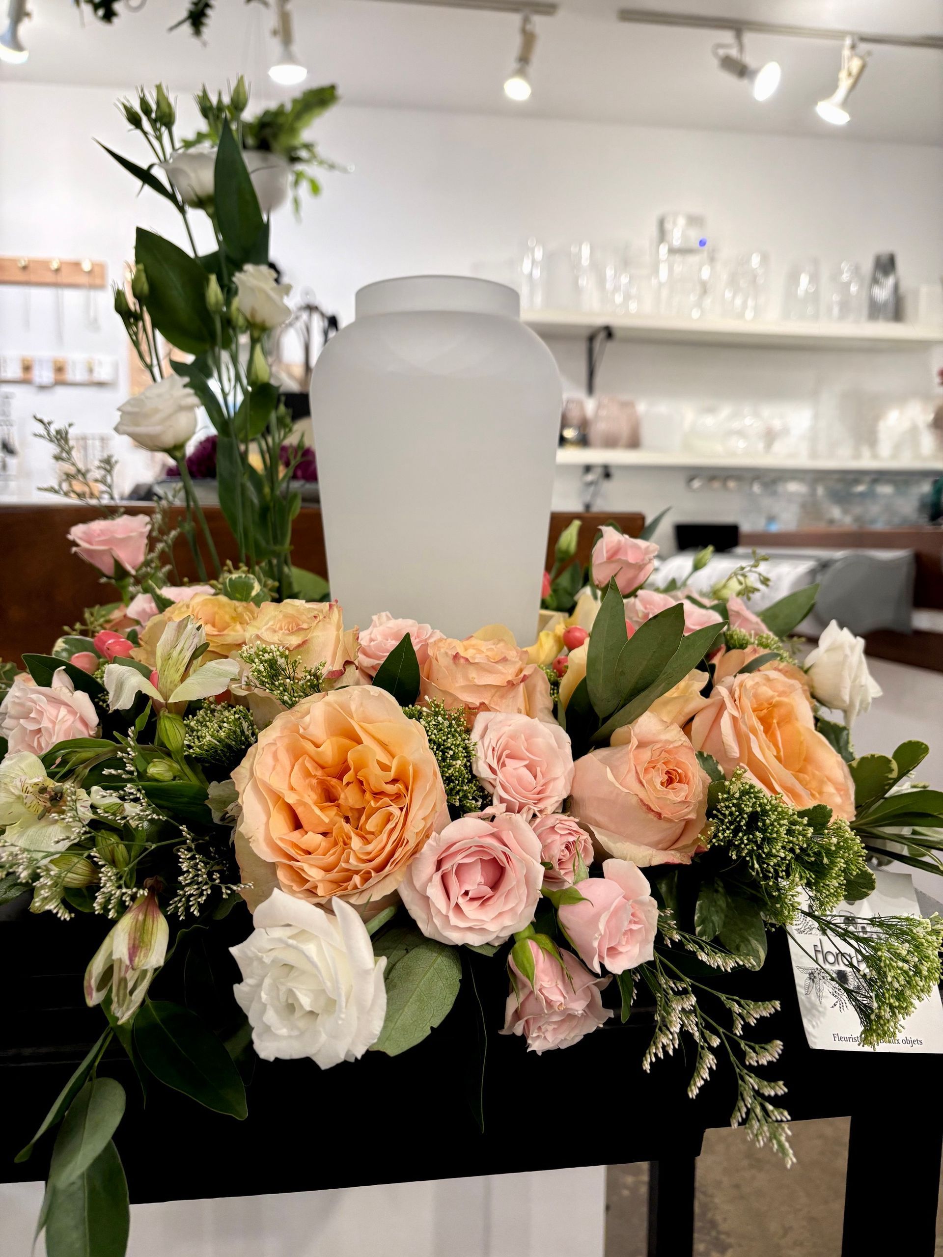 Composition florale funéraire avec des roses pêche et blanches autour d'une urne givrée sur un support noir