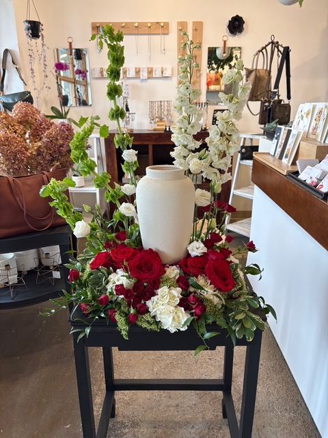 Composition florale dans un vase blanc avec des fleurs rouges et blanches sur un support noir, à l'intérieur d'un magasin