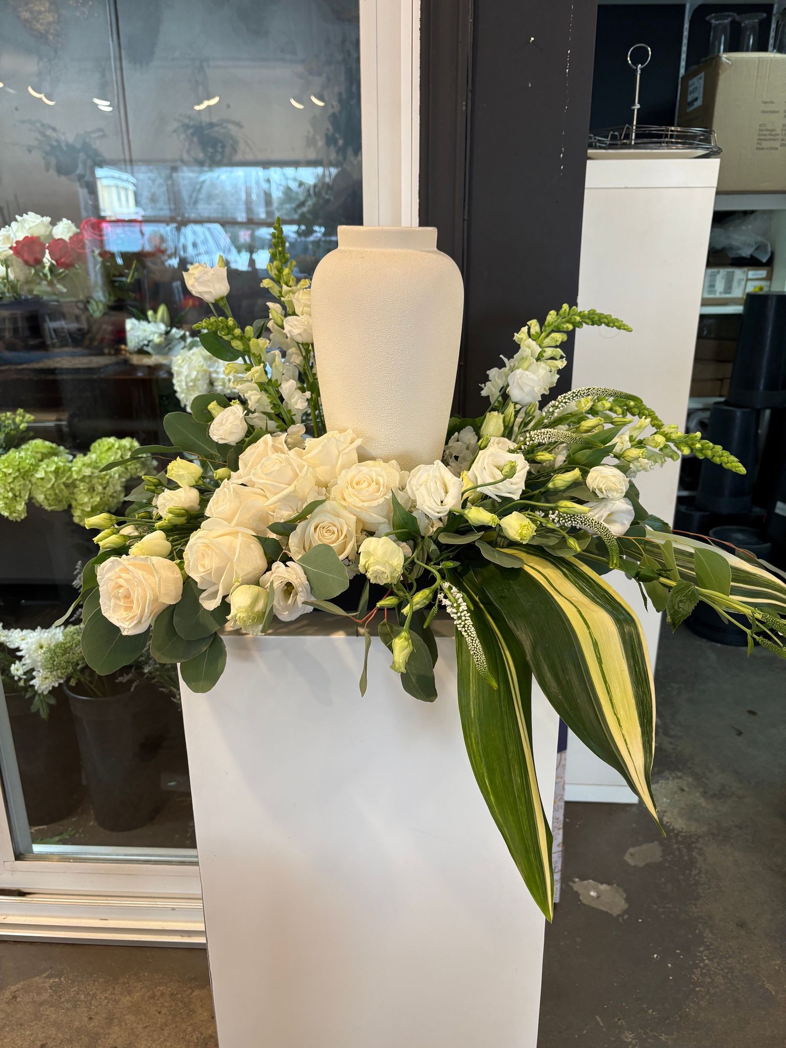 Composition florale funéraire blanche avec une grande bougie sur un support piédestal