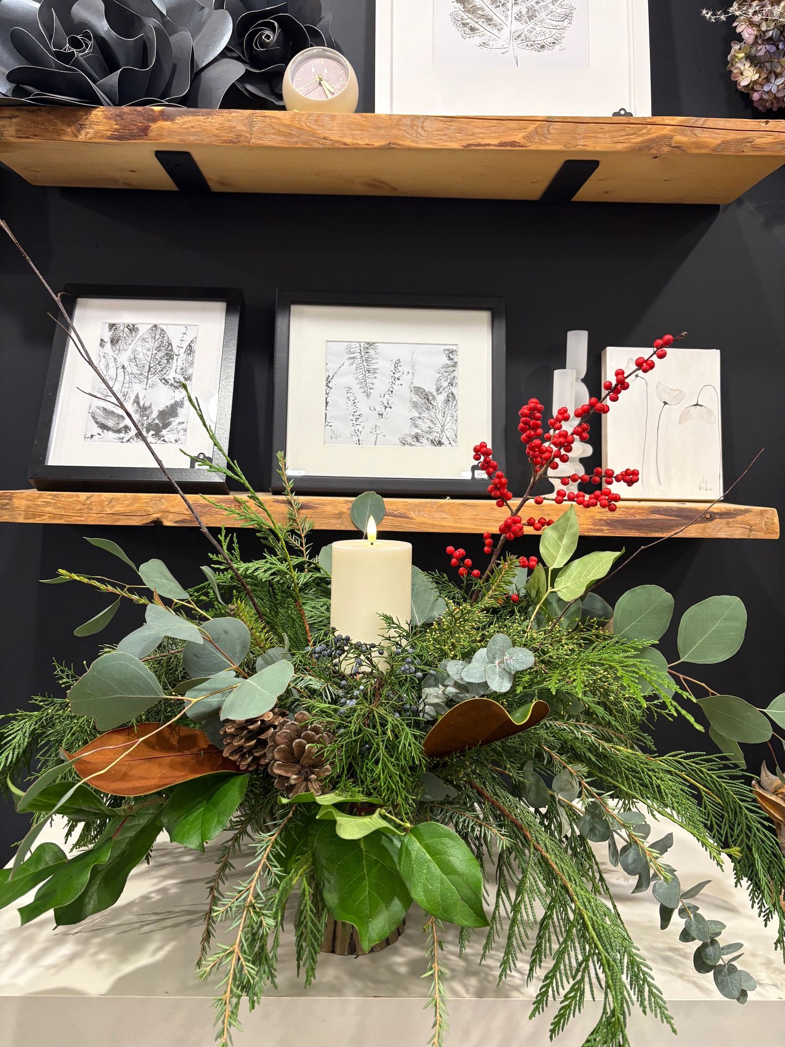 Étagère décorative avec estampes encadrées, verdure, bougies et tiges de baies rouges