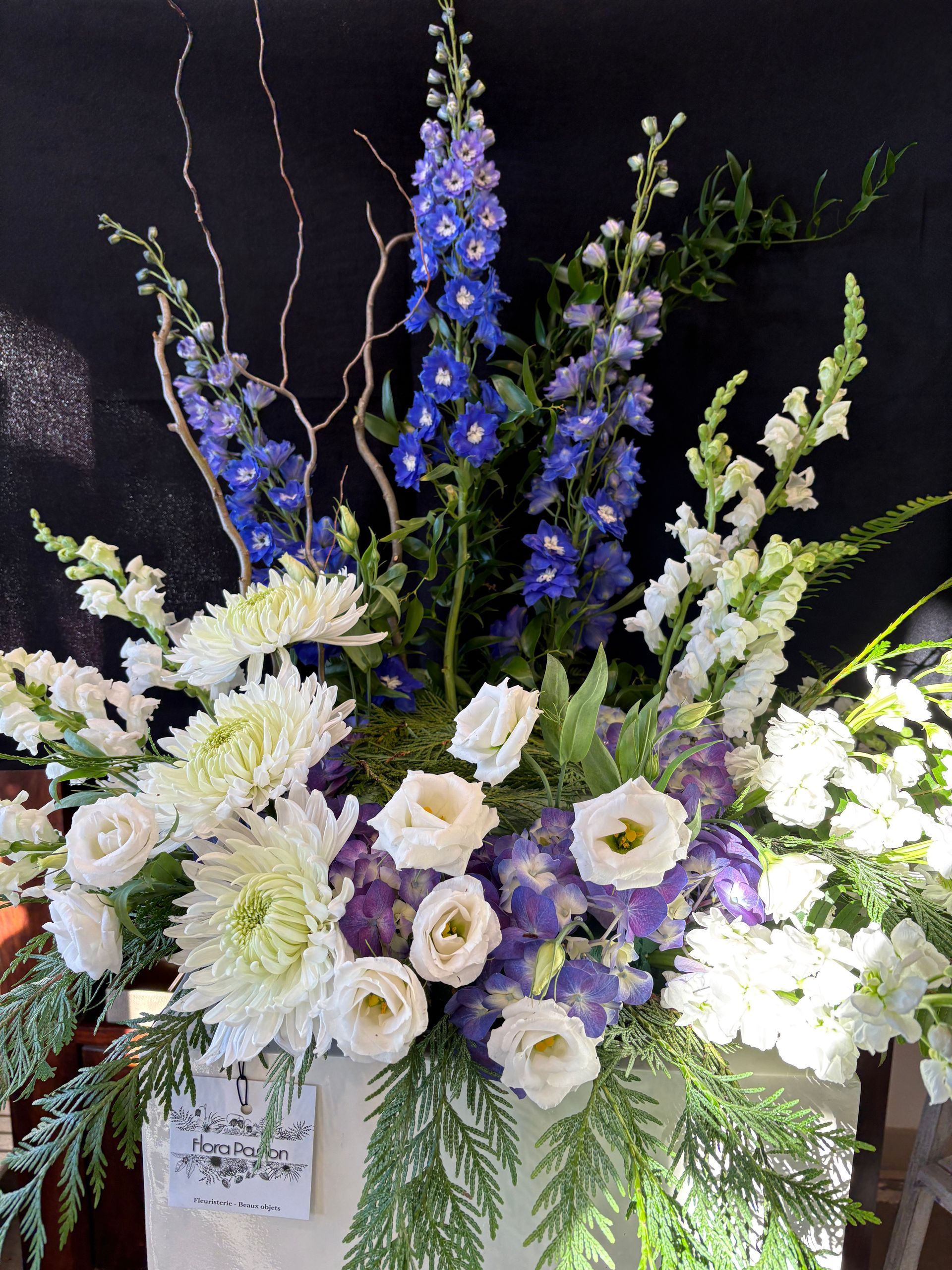 Grande composition florale avec des fleurs bleues, blanches et lavande et de la verdure dans un vase blanc
